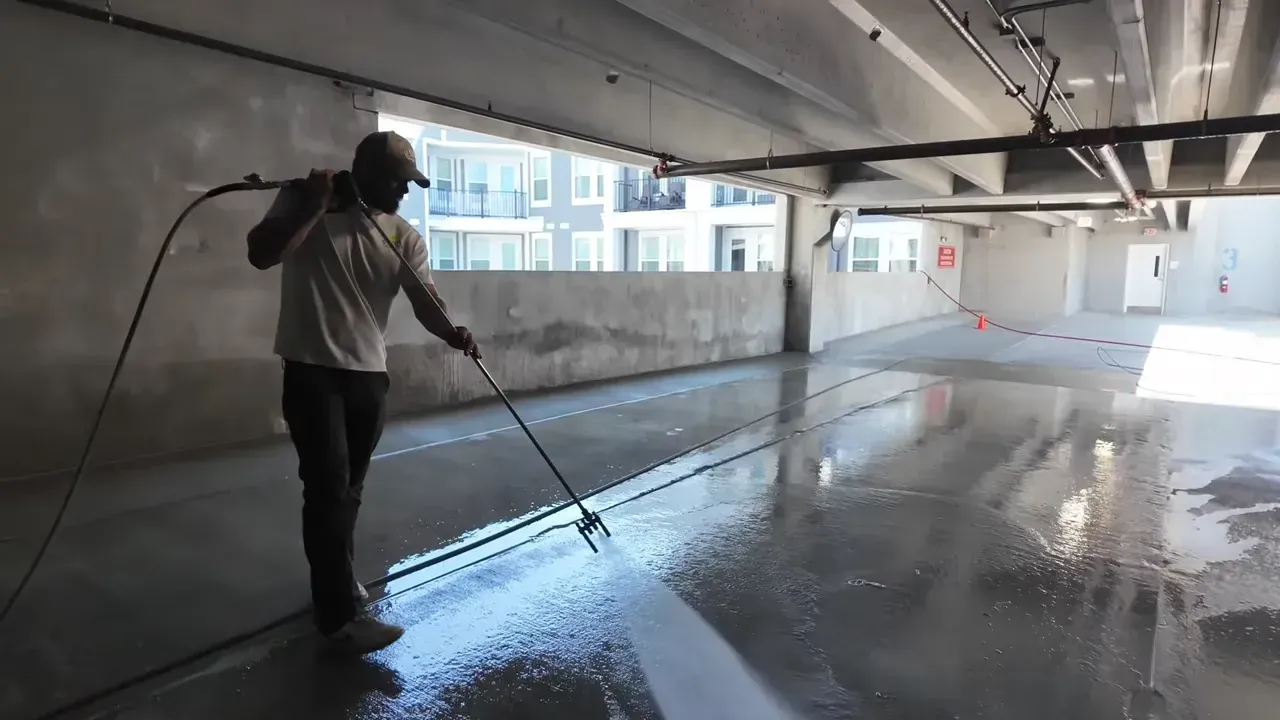 A person spraying sealant on a shiny concrete floor in a parking garage.