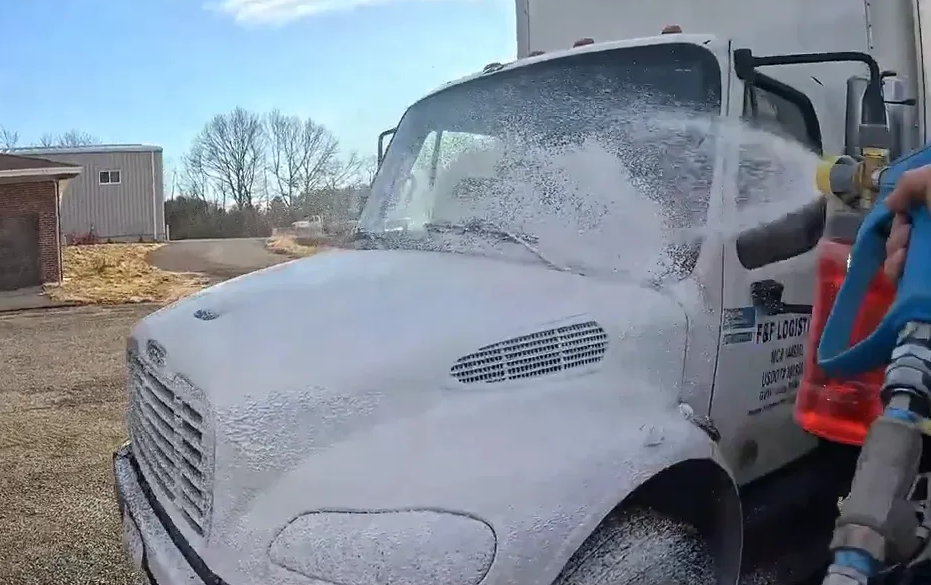 Truck being washed with foamy soap. Outdoor setting, daylight.