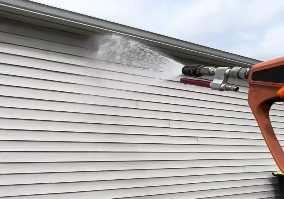 Pressure washer spraying water on white siding.