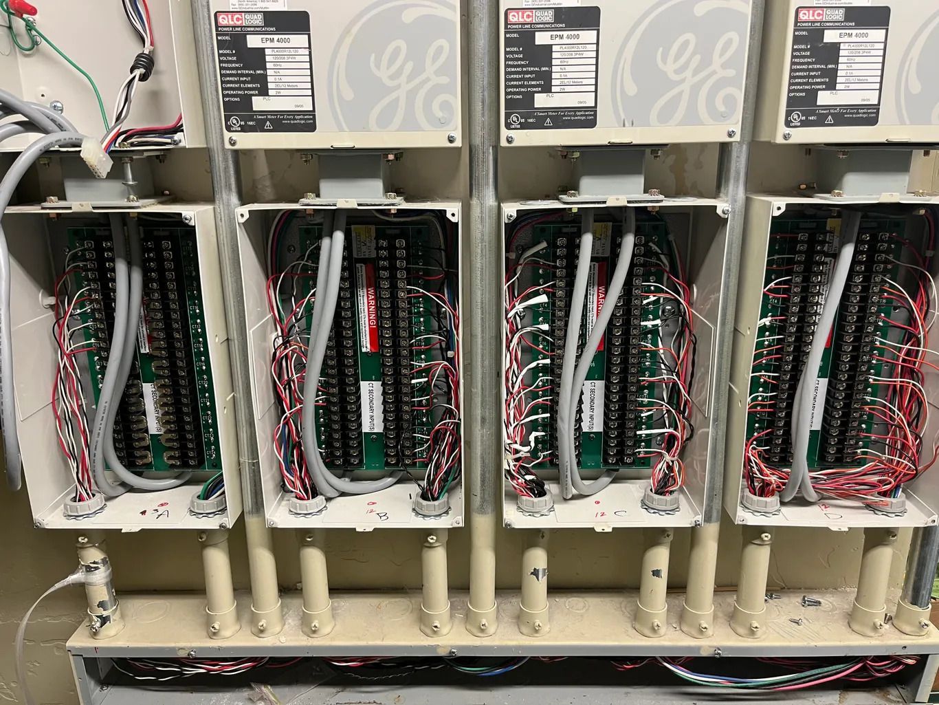 Four open electrical boxes with circuit boards and wiring, mounted on a wall. The boxes are cream-colored with GE logos.