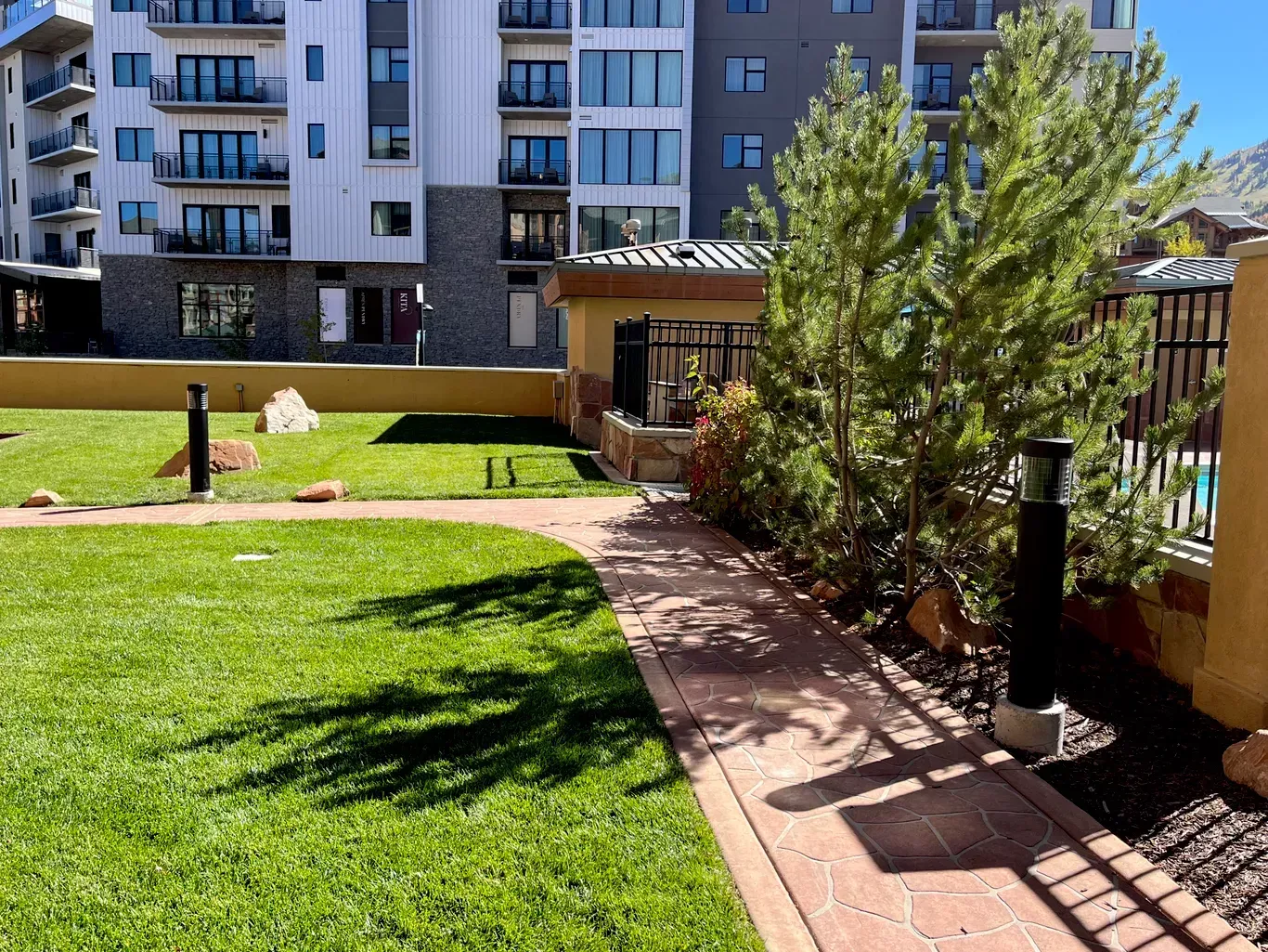 Green lawn and brick path lead to a building with balconies.