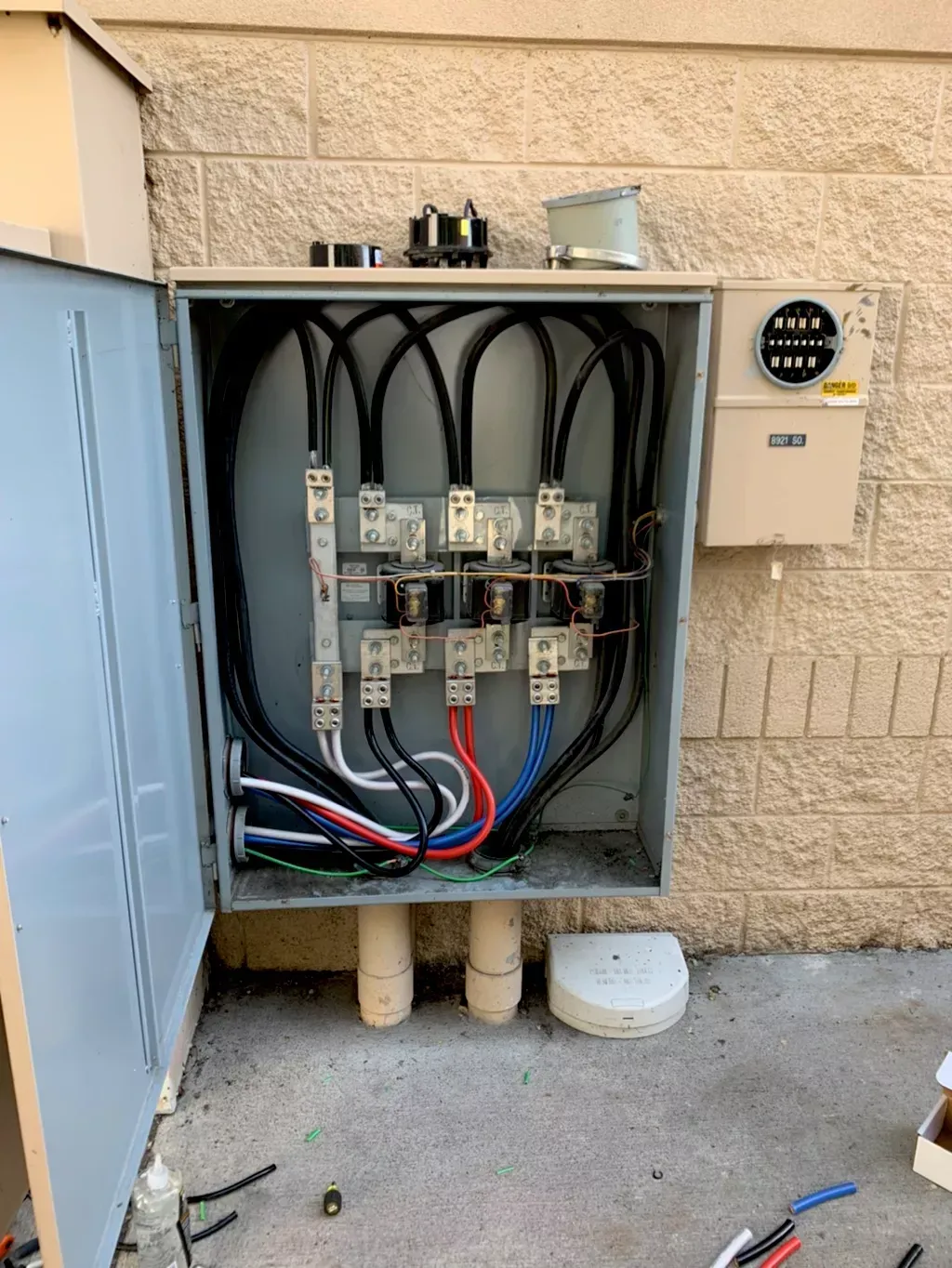 Exterior electrical box with open door, showing wires and components against a beige brick wall.