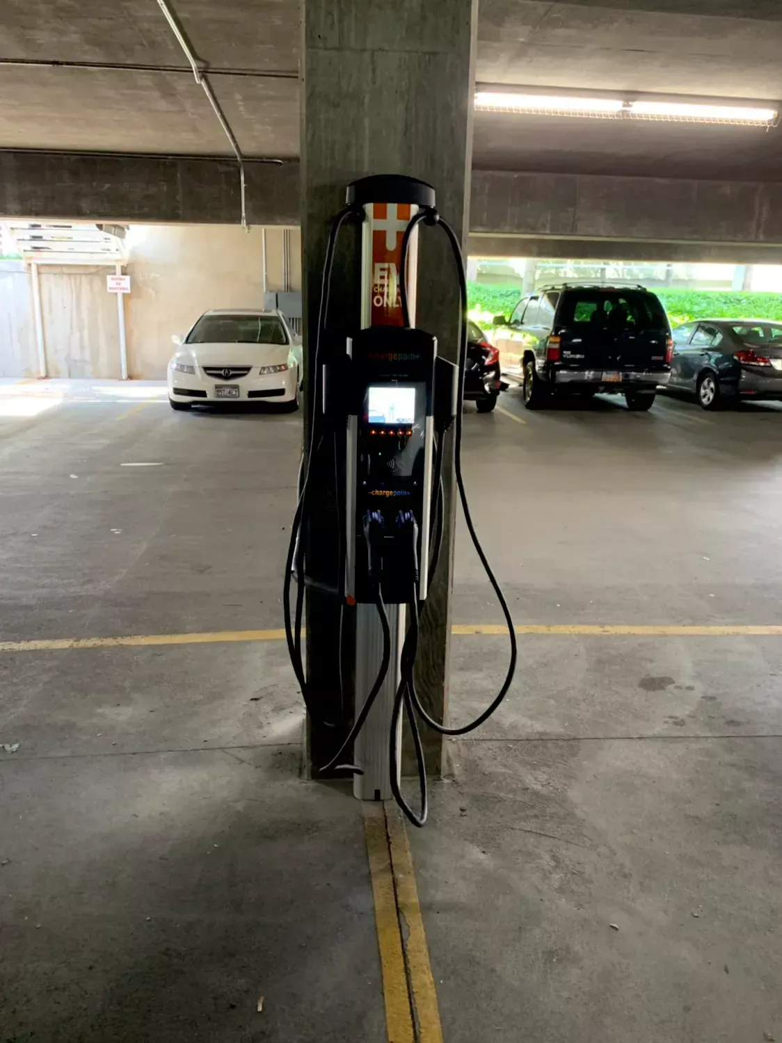 EV charging station on a concrete pillar in a parking garage; cables hang down.