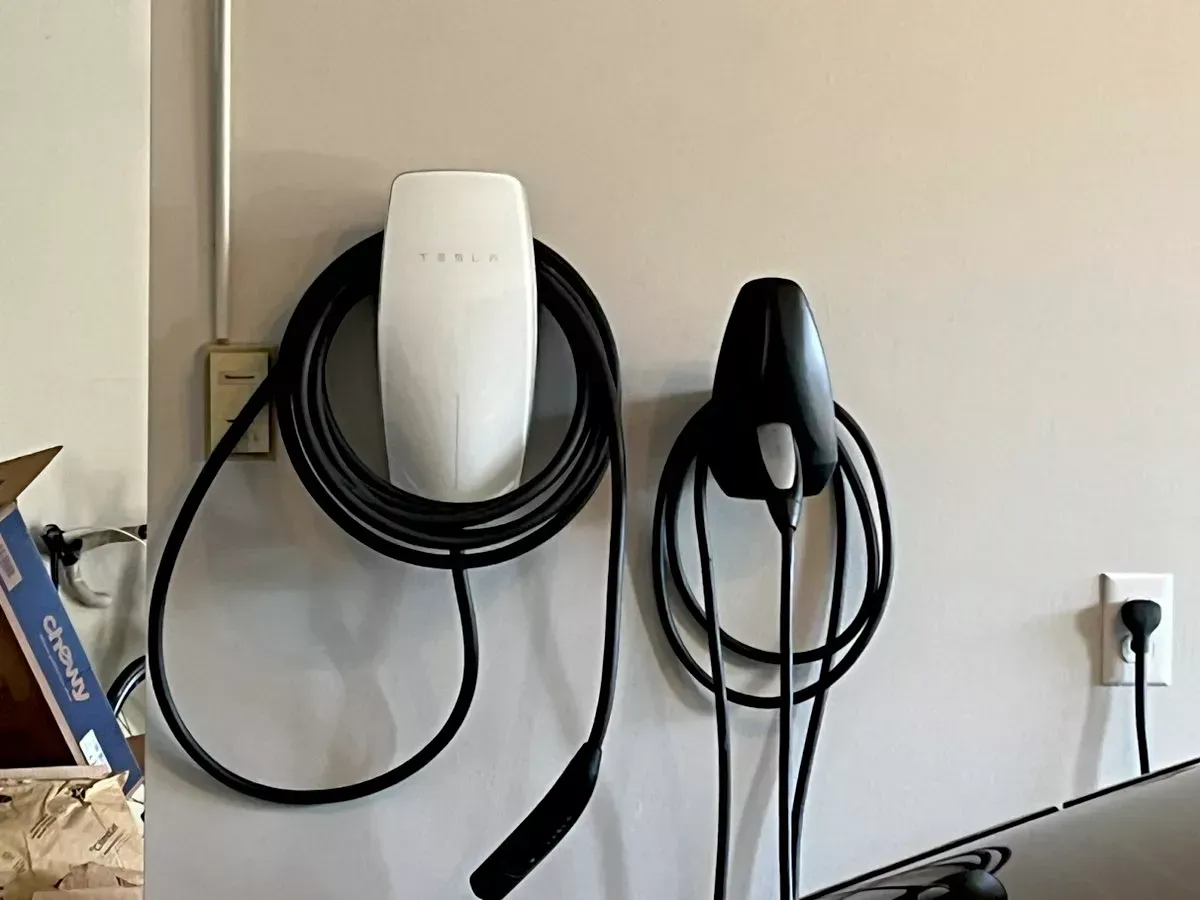 Two EV chargers mounted on a light-colored wall, one white and one black, with their charging cables coiled.
