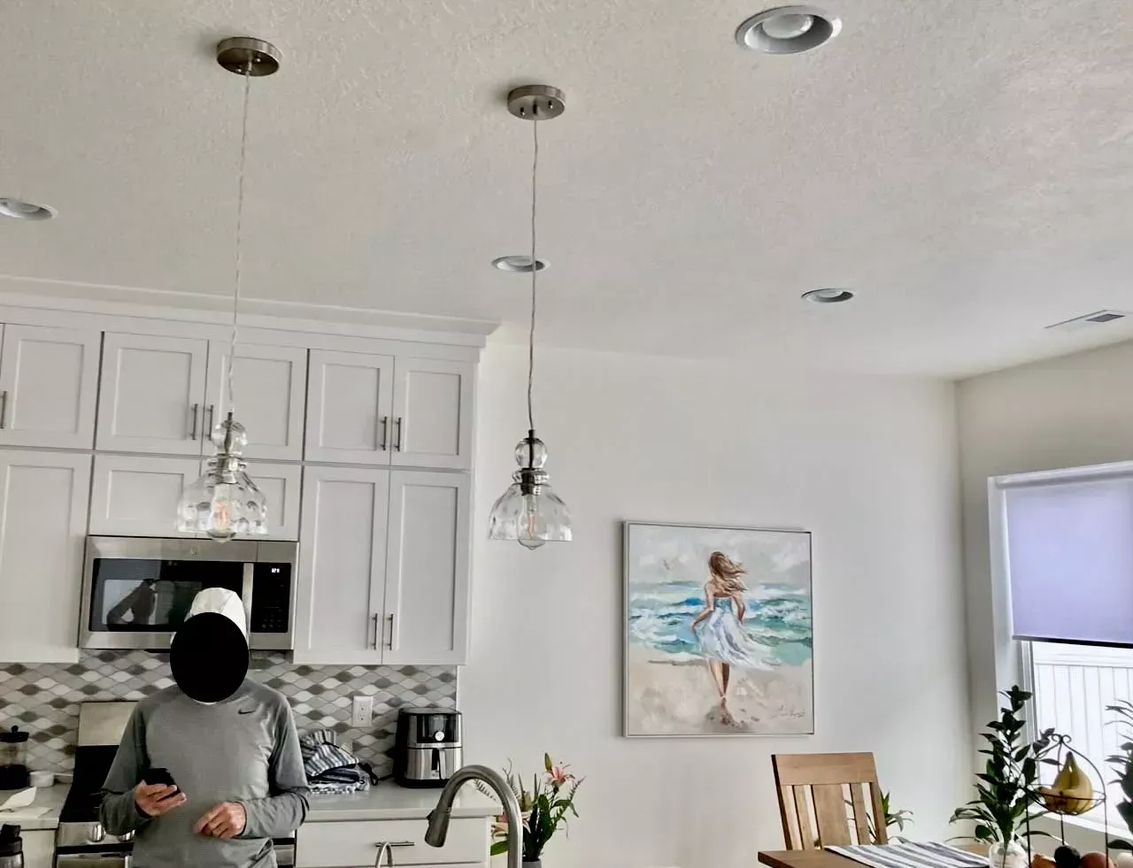 A ceiling with a decorative light fixture, recessed light, and smoke detector. A framed art piece of greenery hangs below.