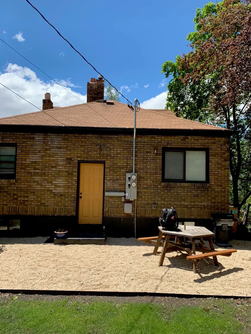 Back of a brick house with a yellow door, a picnic table, and gravel patio against a blue sky.