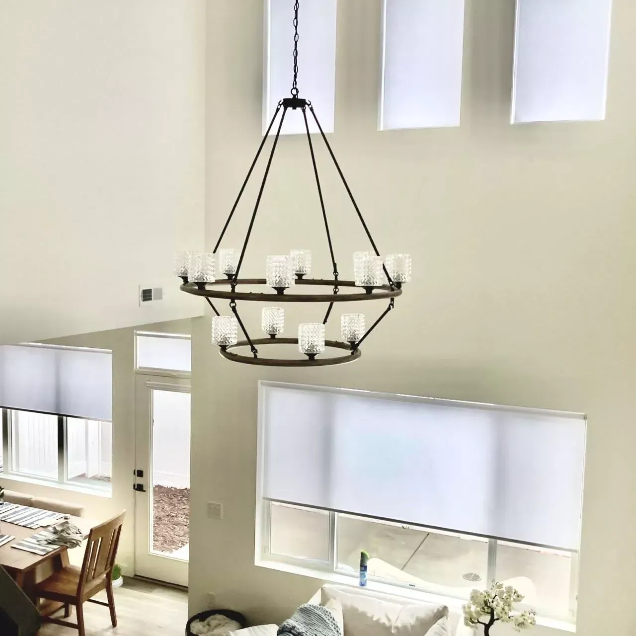 Large chandelier hanging in a two-story room with white walls, windows, and blinds.