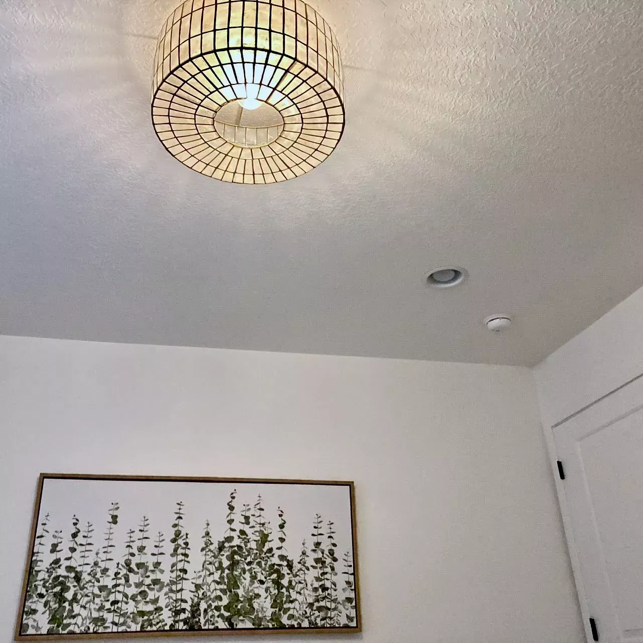 A room with a round ceiling light, artwork, and a door.