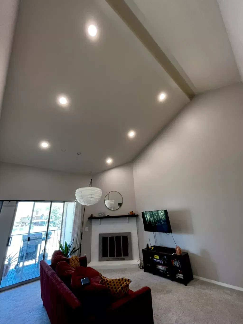 Living room with vaulted ceiling, recessed lights, fireplace, TV, and red sofa.