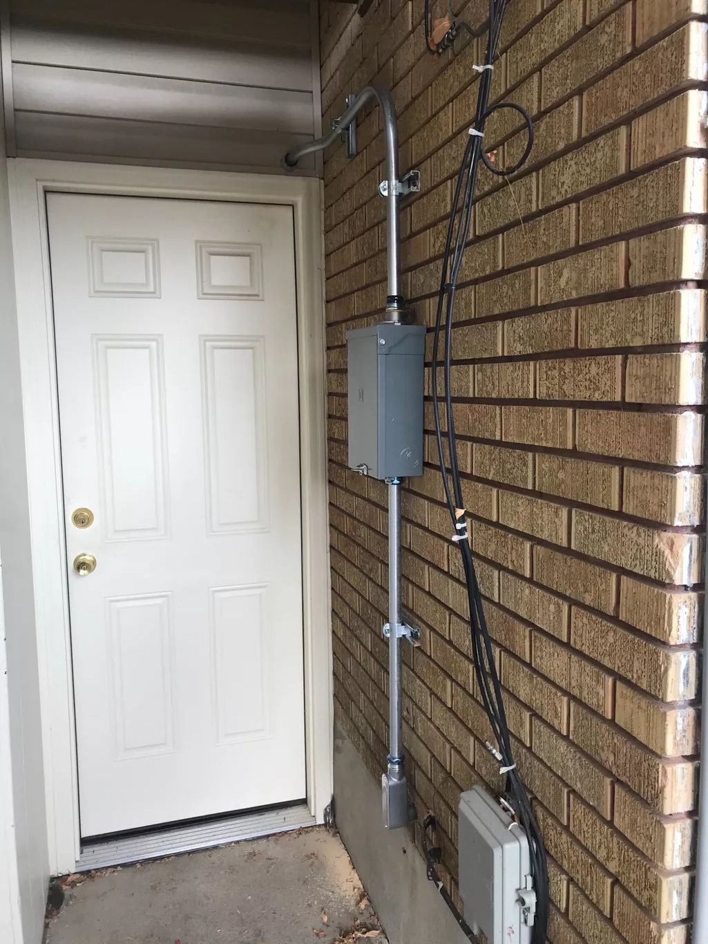 White door next to brick wall with utility equipment attached, including a metal box and conduit.