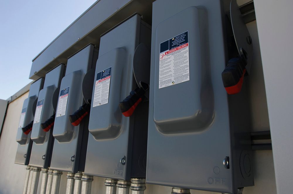 Gray electrical boxes with red handles mounted on a wall, outdoors.