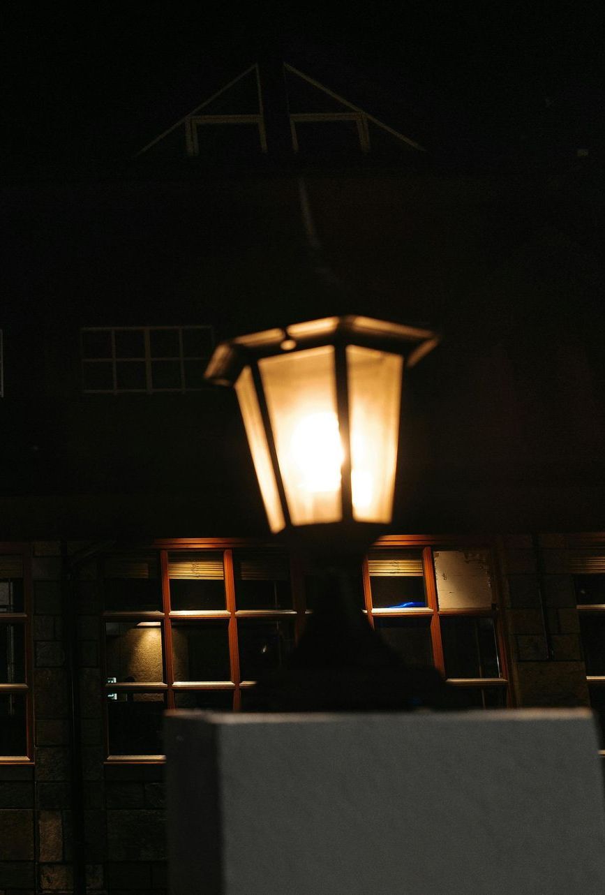 Glowing outdoor lamp post at night, in front of a dark building.