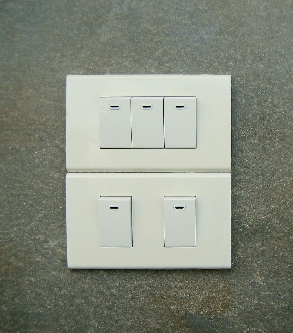Two white light switch plates with toggle switches on a gray wall.