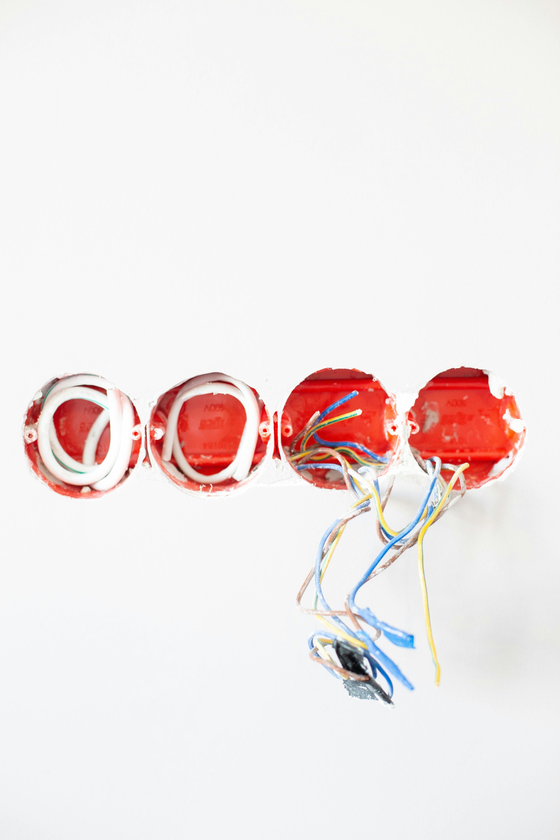 Four red electrical boxes in white wall with wires protruding.