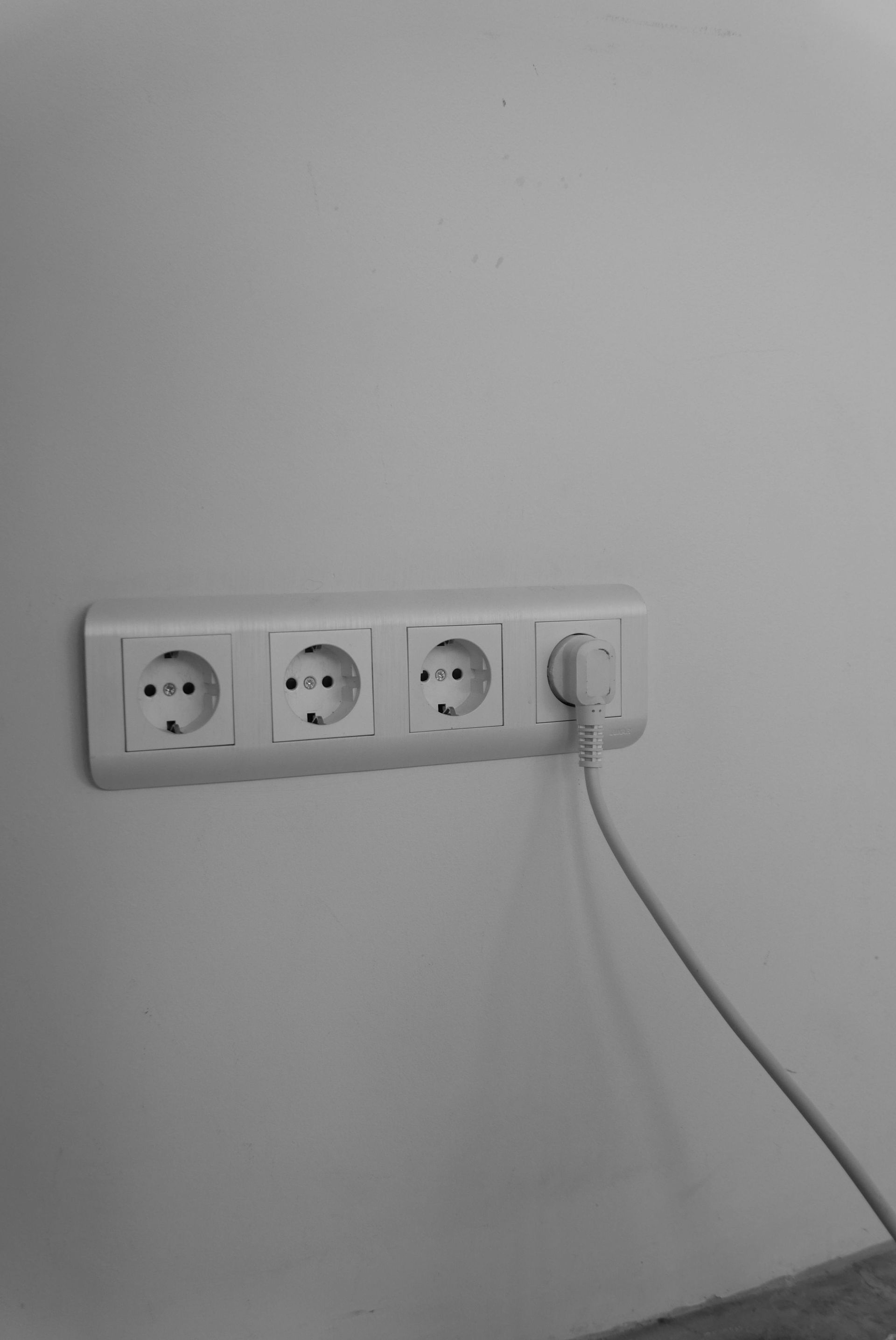 Four white electrical outlets on a white wall, with a cord plugged into one.