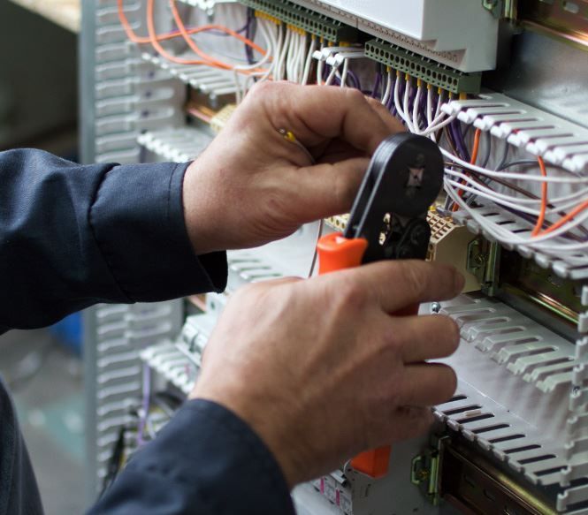 Hands of an electrician wiring a control panel with orange crimping tool.