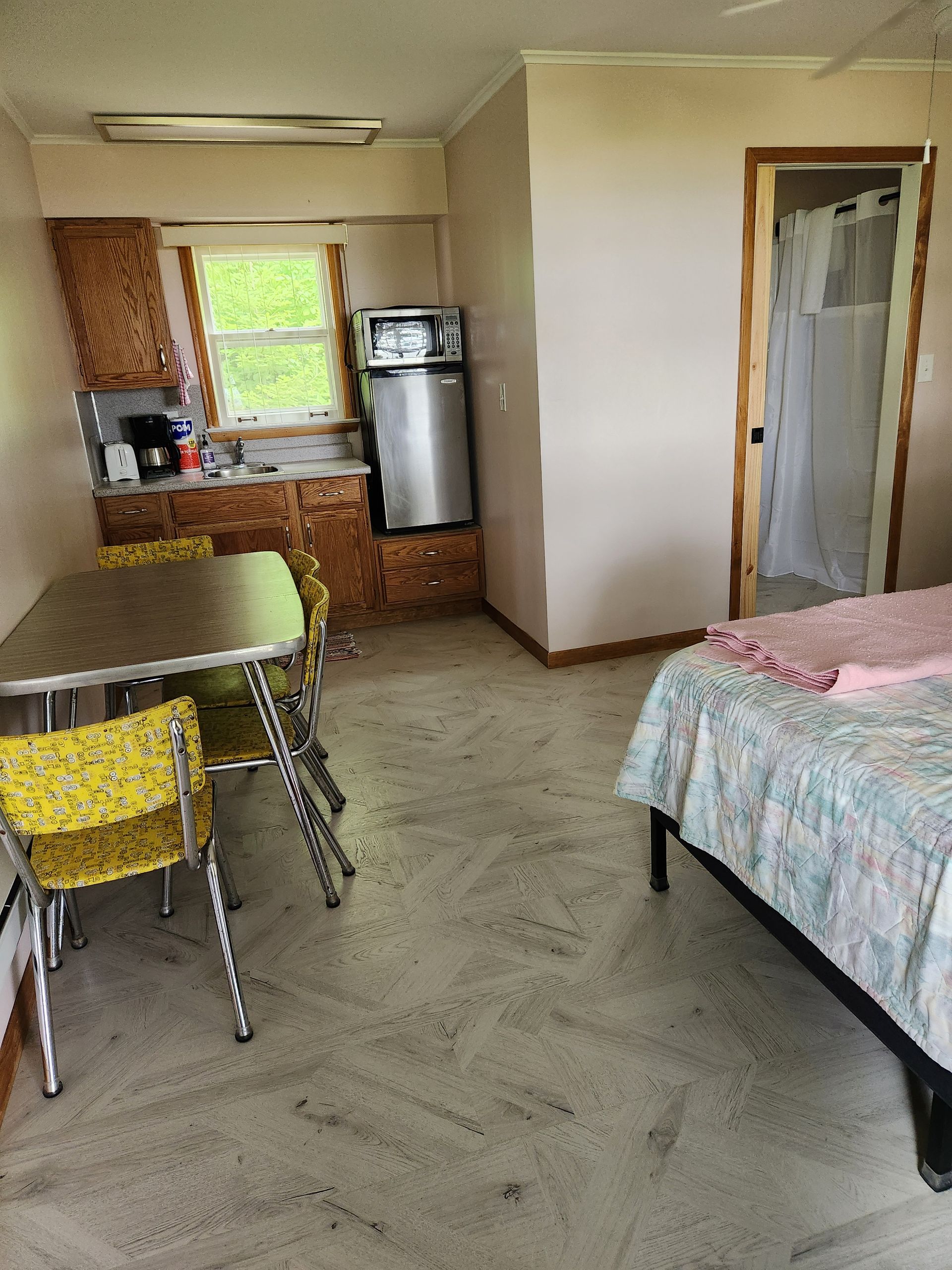 Small motel room with kitchen, dining area, bed, and bathroom door.