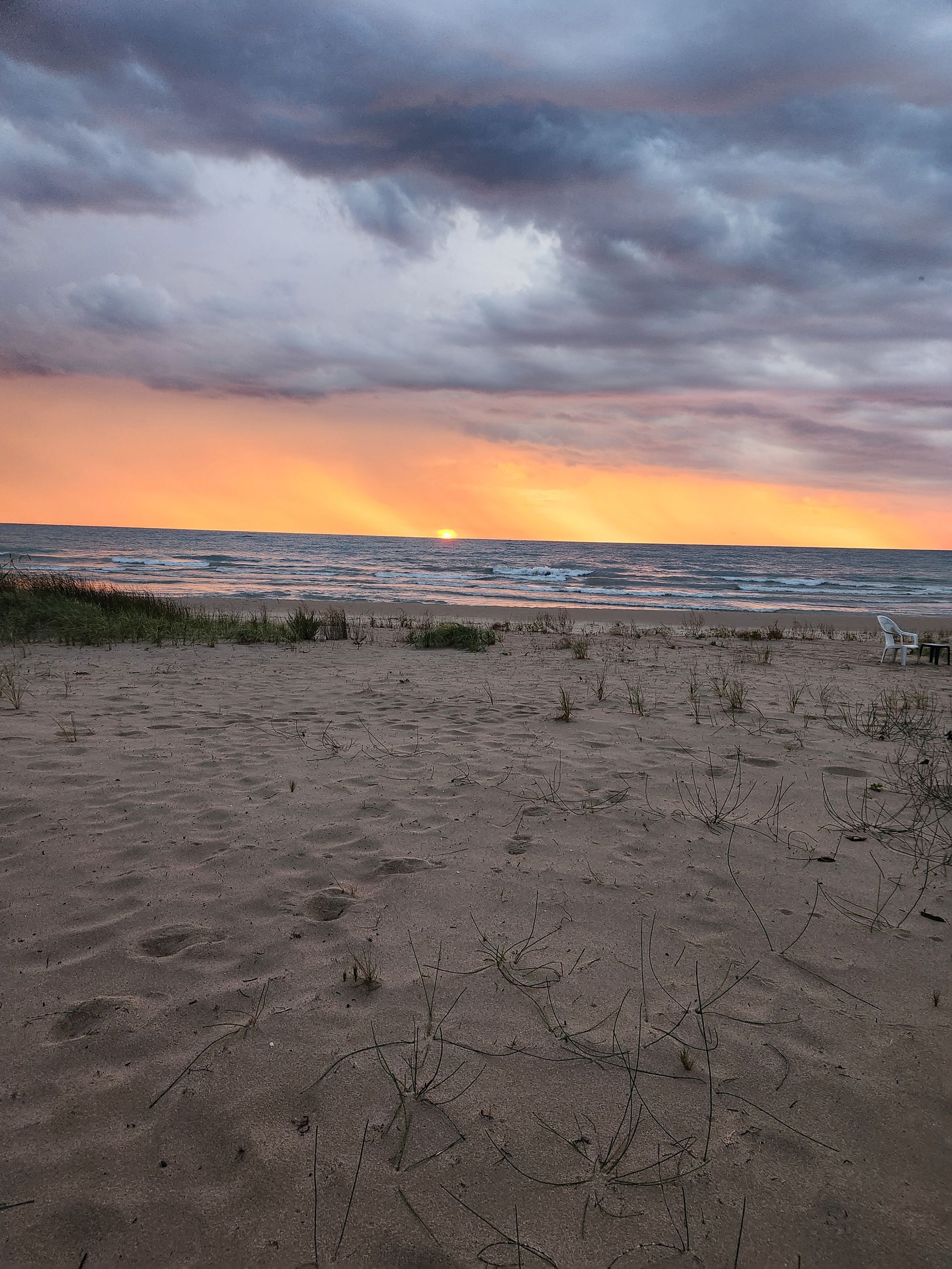 Beach scene at sunset. Orange and yellow sky above choppy water. Dark sand in foreground.