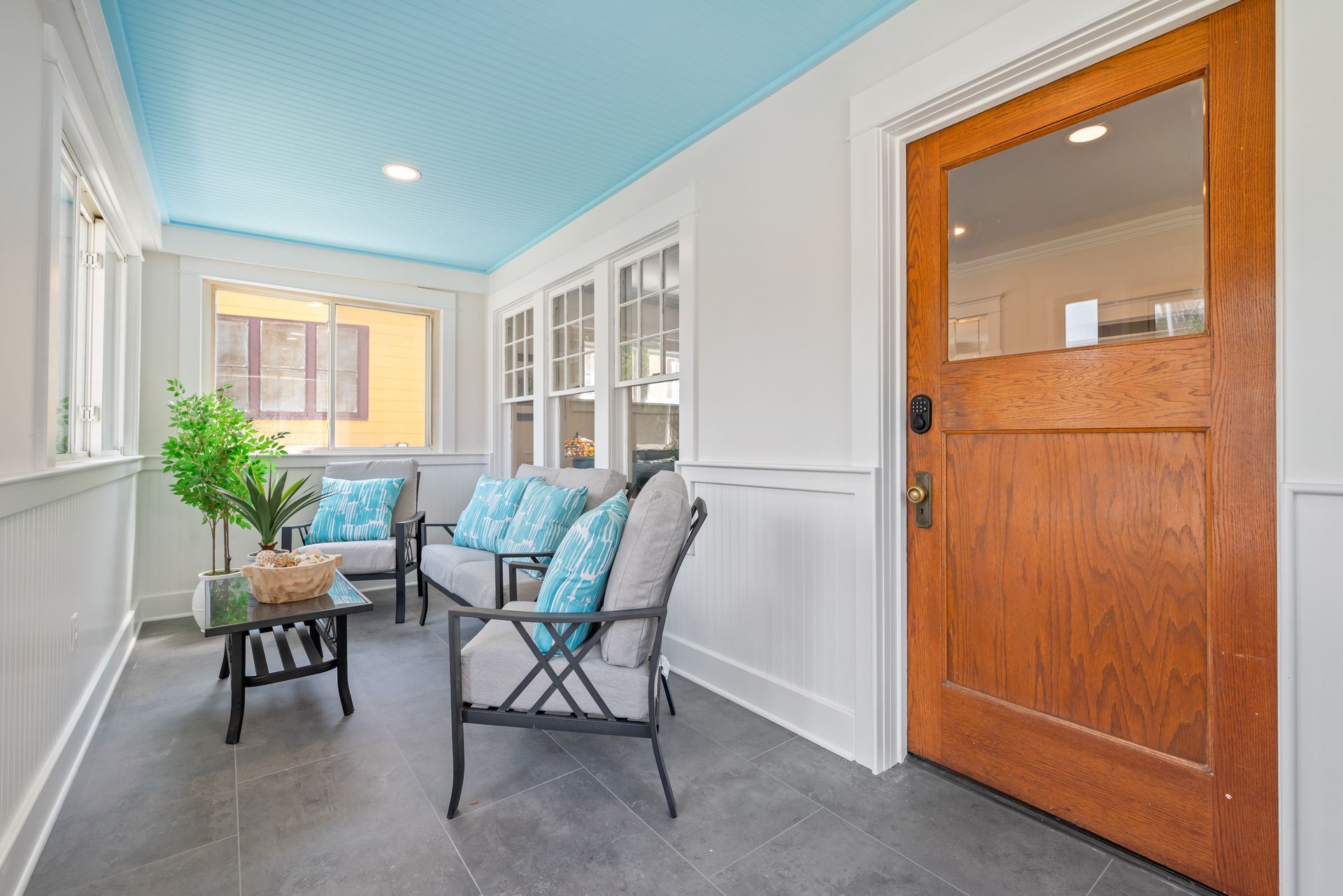 Sunroom with blue ceiling, seating, and wooden door.