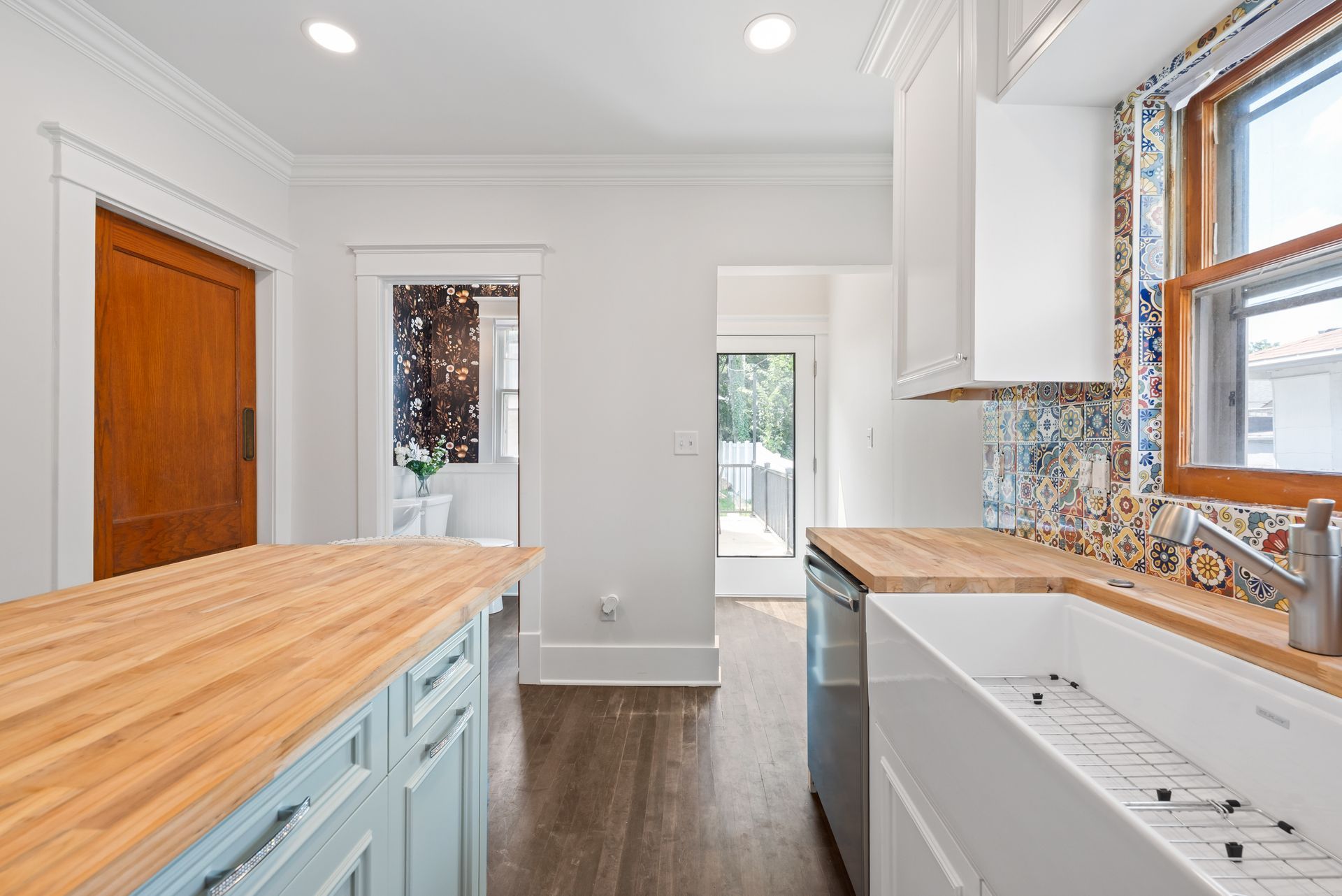 Kitchen with light blue island, butcher block counters, white sink, and patterned backsplash.