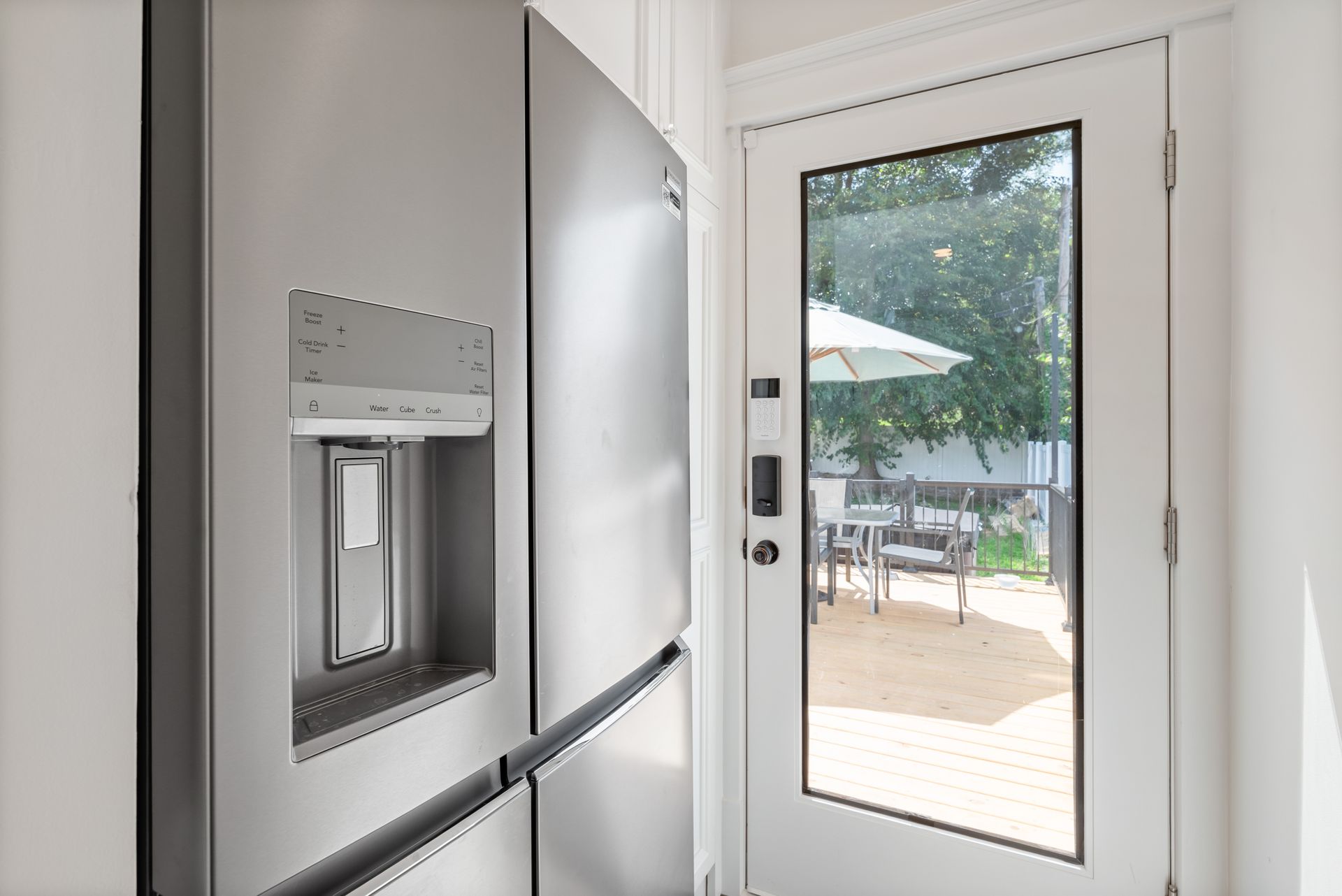 Stainless steel refrigerator next to a glass door leading to an outdoor patio with umbrella and furniture.
