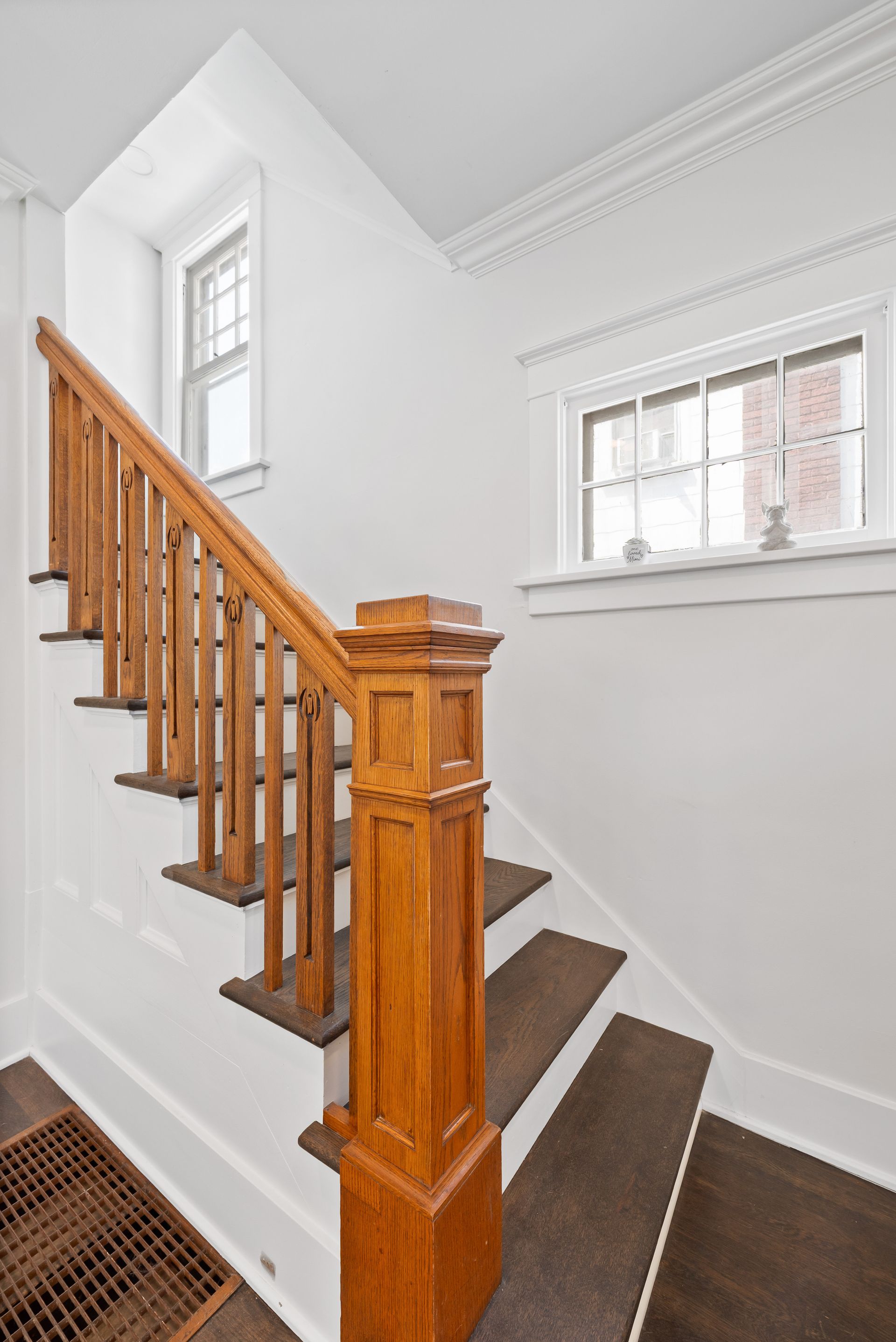 Wooden staircase with brown treads and railing, white walls, two small windows.