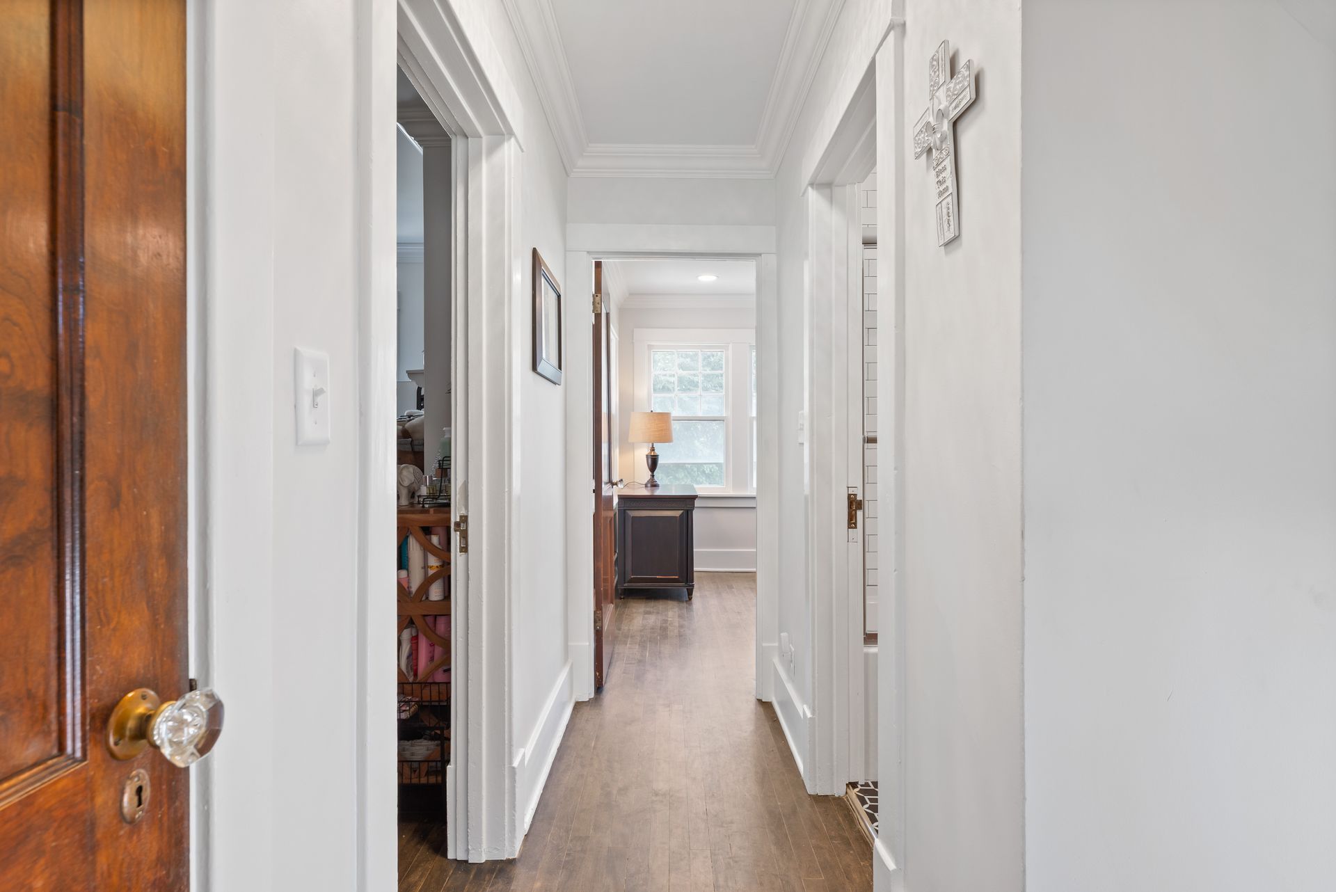 Narrow hallway with white walls, dark wood floor, and three open doorways.