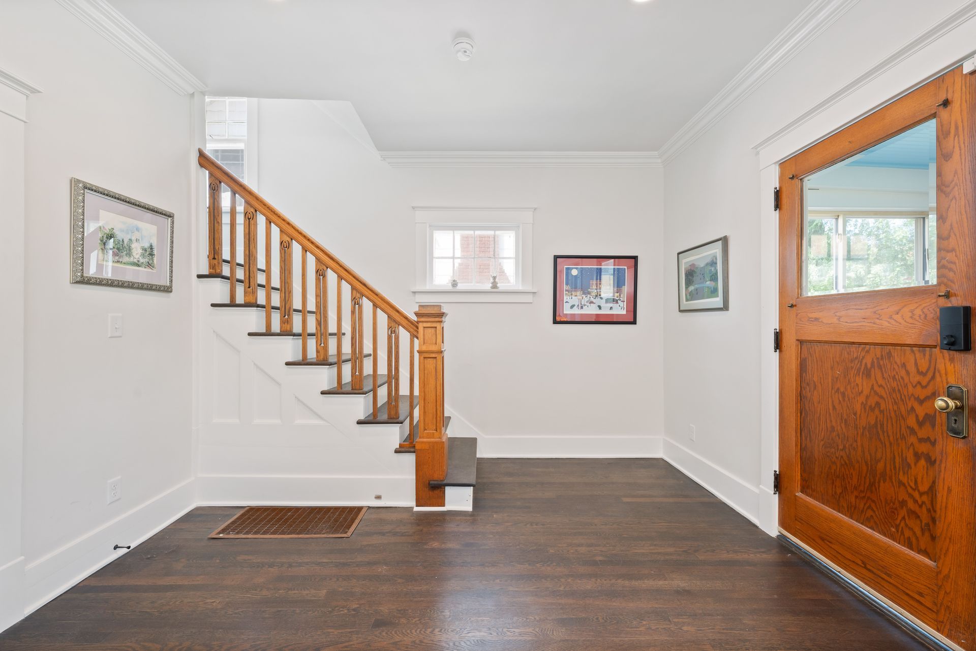 Entryway with wooden door, staircase, dark hardwood floors, and white walls.