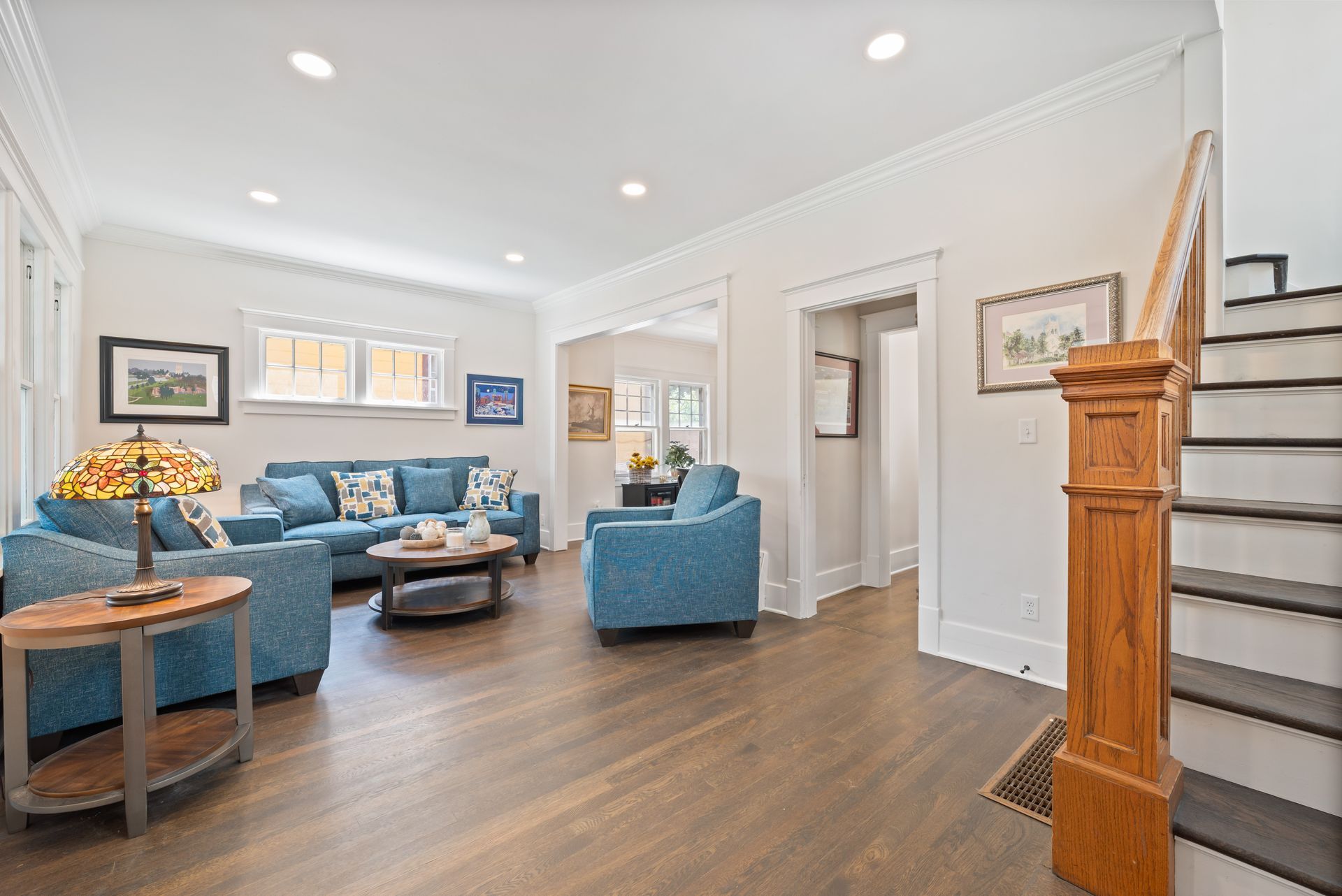 Bright living room with blue furniture and hardwood floors. Staircase on the right.