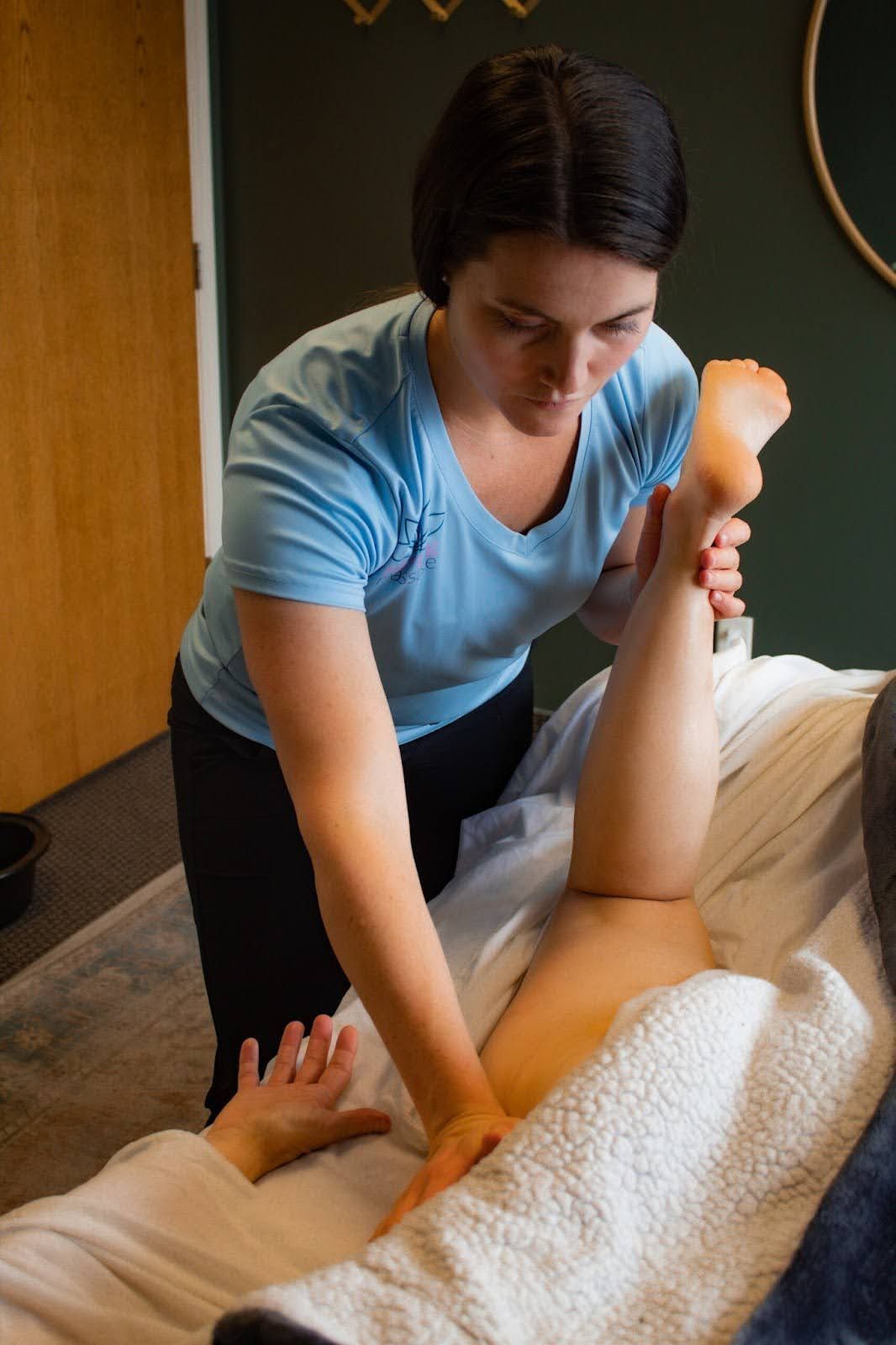 A woman is giving a massage to a person laying on a bed.