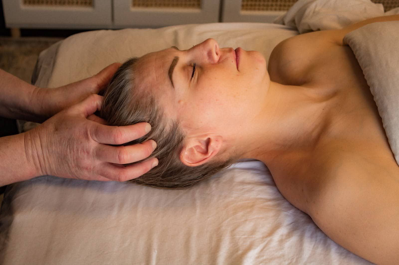 A woman is laying on a bed getting a head massage.