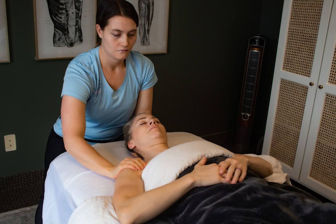 A woman is giving a massage to a woman laying on a massage table.