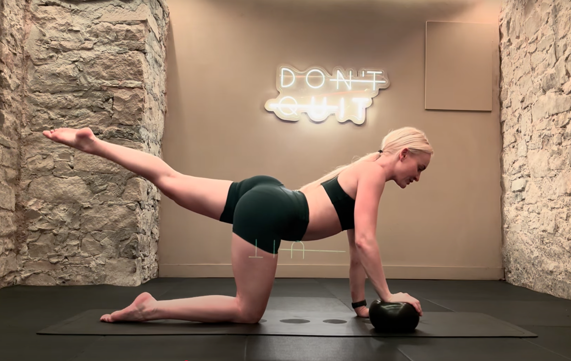Woman in a yoga pose, side plank with an arm raised up. She is in a room with stone walls, lit by candles and a neon sign.