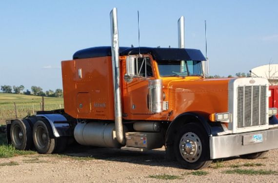 A large orange semi truck is parked in a gravel lot.