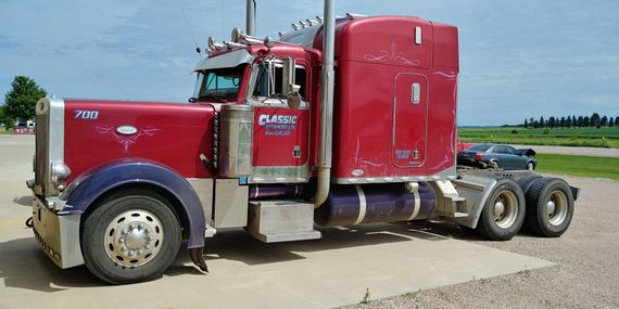 A red semi truck is parked in a gravel lot.