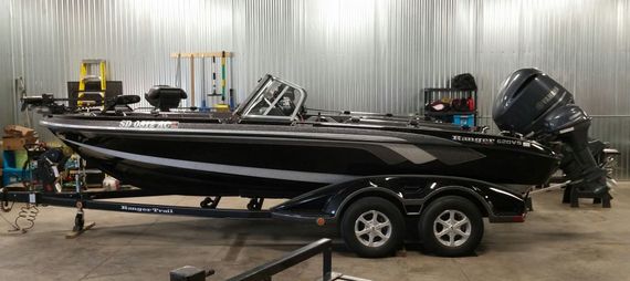 A black fishing boat is parked on a trailer in a garage.
