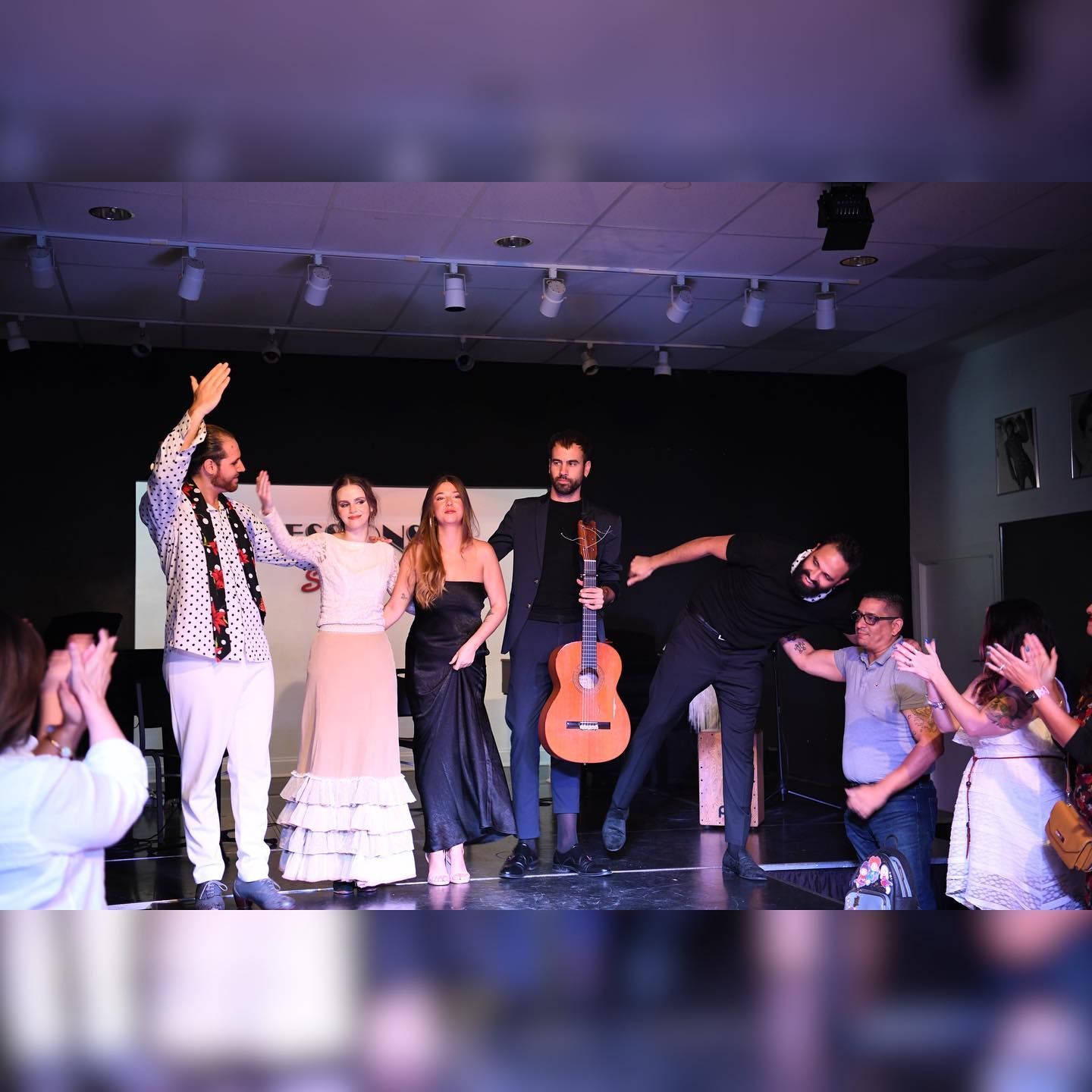 A group of people are standing on a stage with a man holding a guitar.