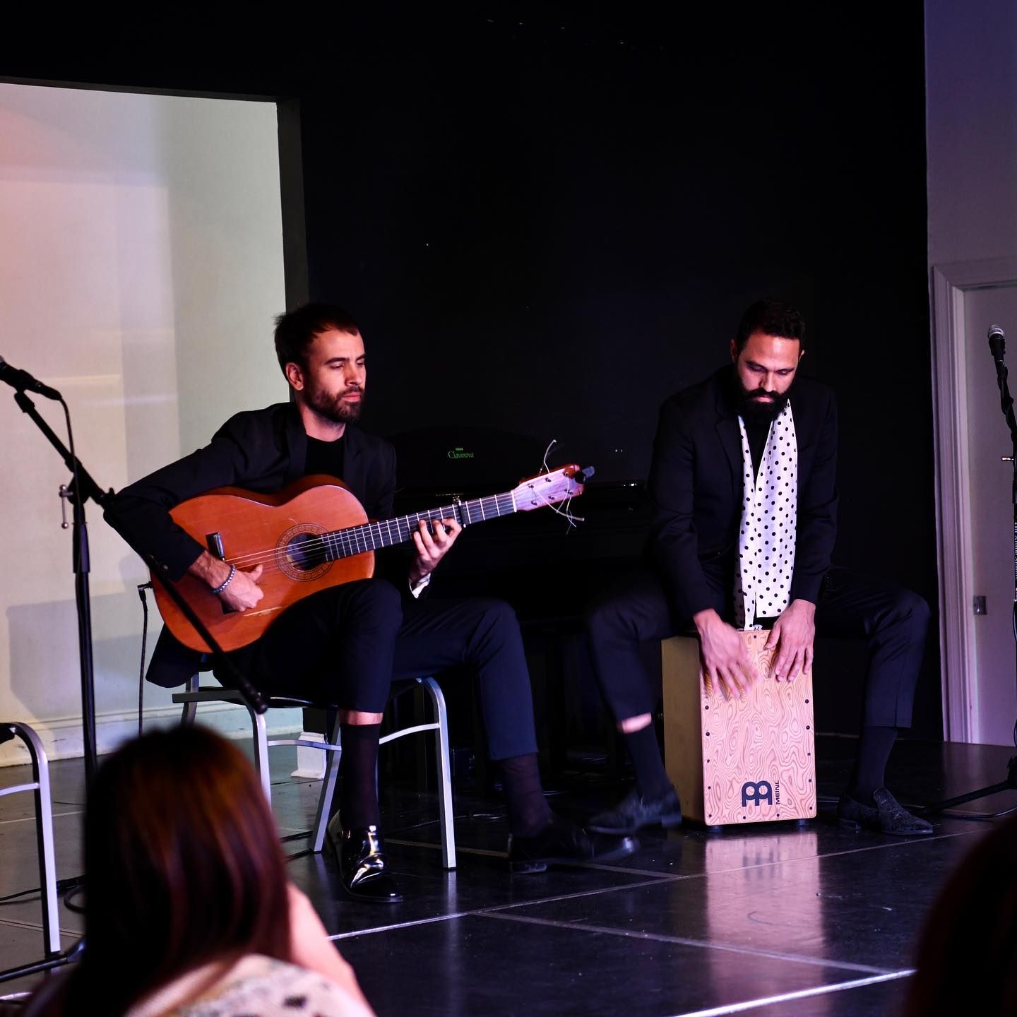 A man playing a guitar next to another man playing a cajon