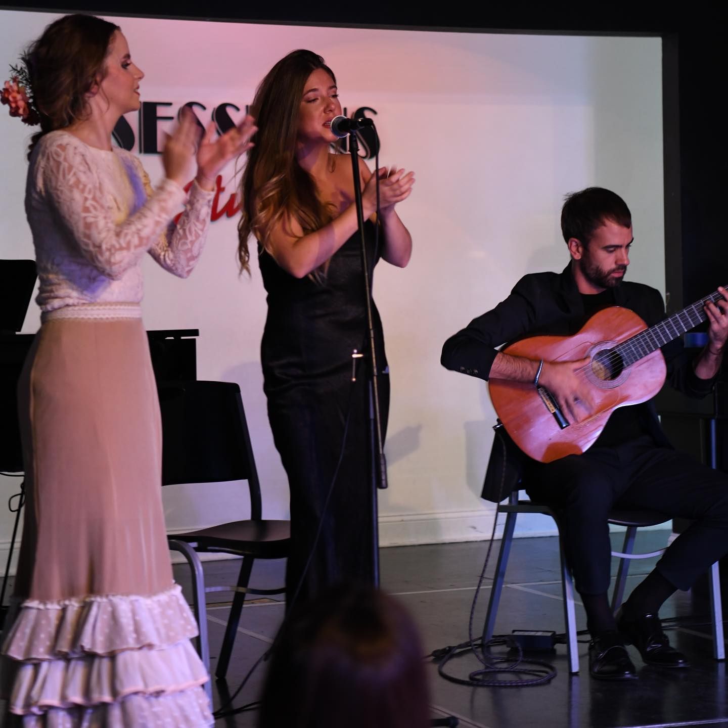 A woman singing into a microphone while a man plays a guitar
