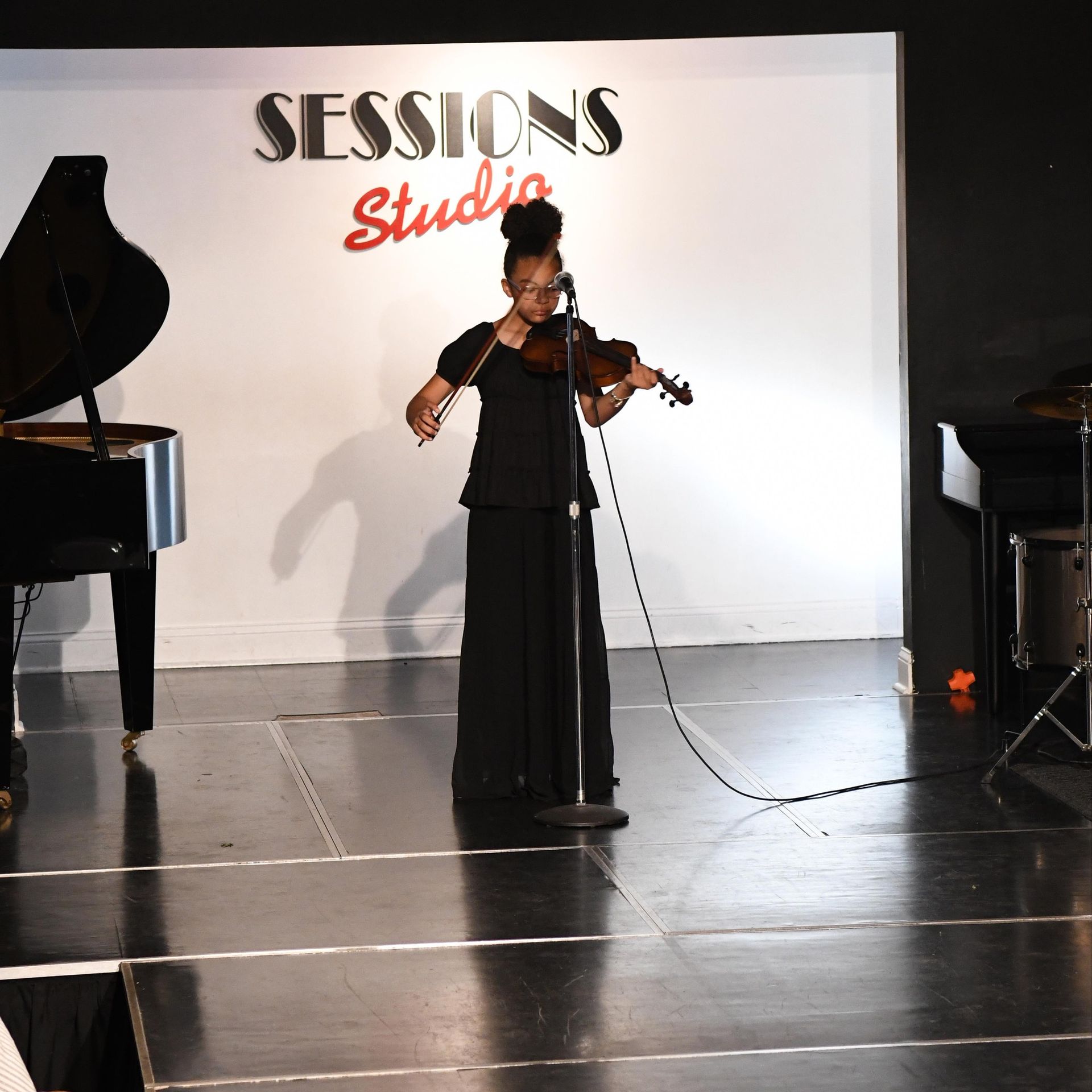 A woman playing a violin in front of a sign that says sessions studio