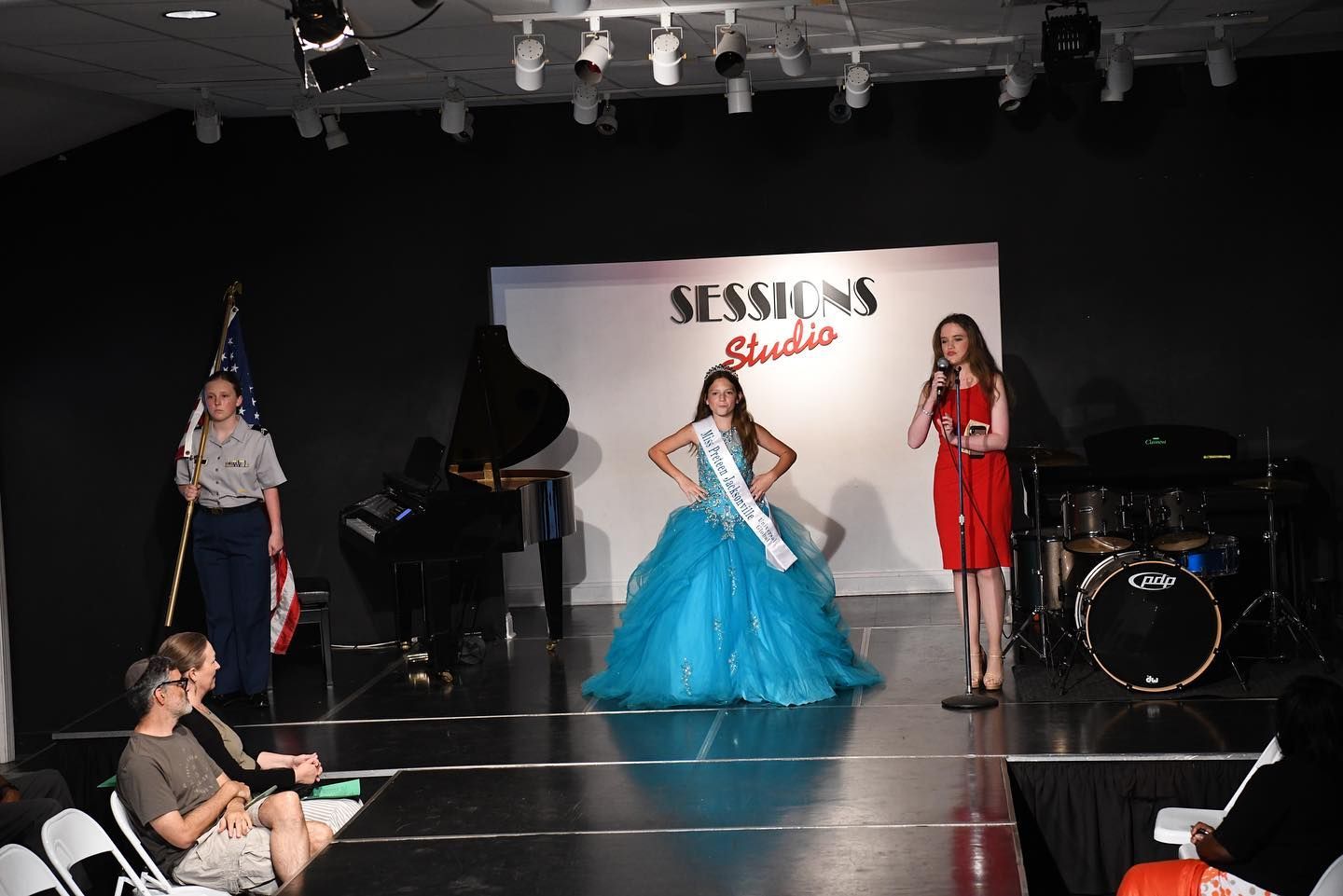 A woman in a blue dress is standing on a stage in front of a sign that says sessions studio