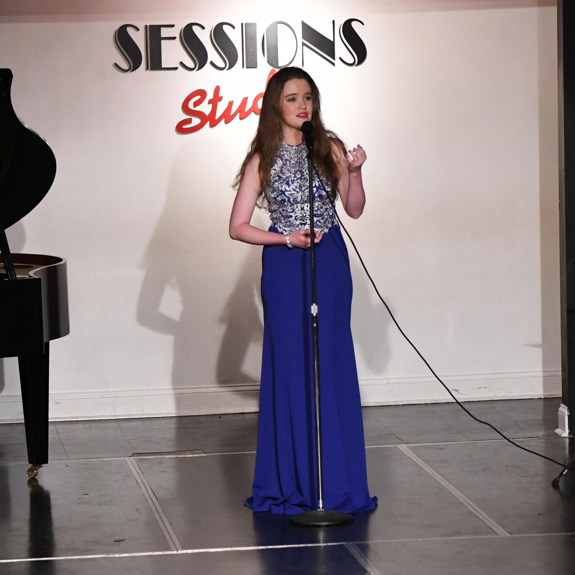 A woman singing into a microphone in front of a sign that says sessions studio