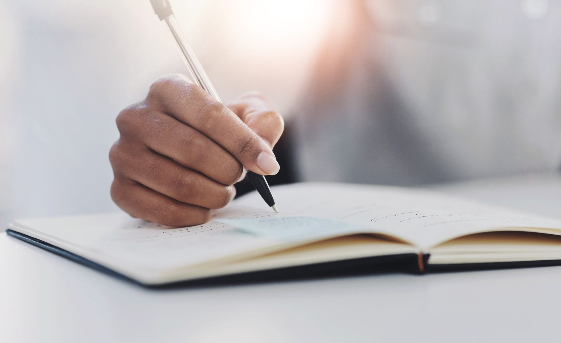 Person writing in a notebook with a pen at a desk.