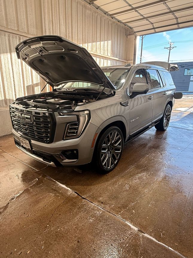 A silver SUV with its hood open parked inside a wet, industrial-style garage bay.