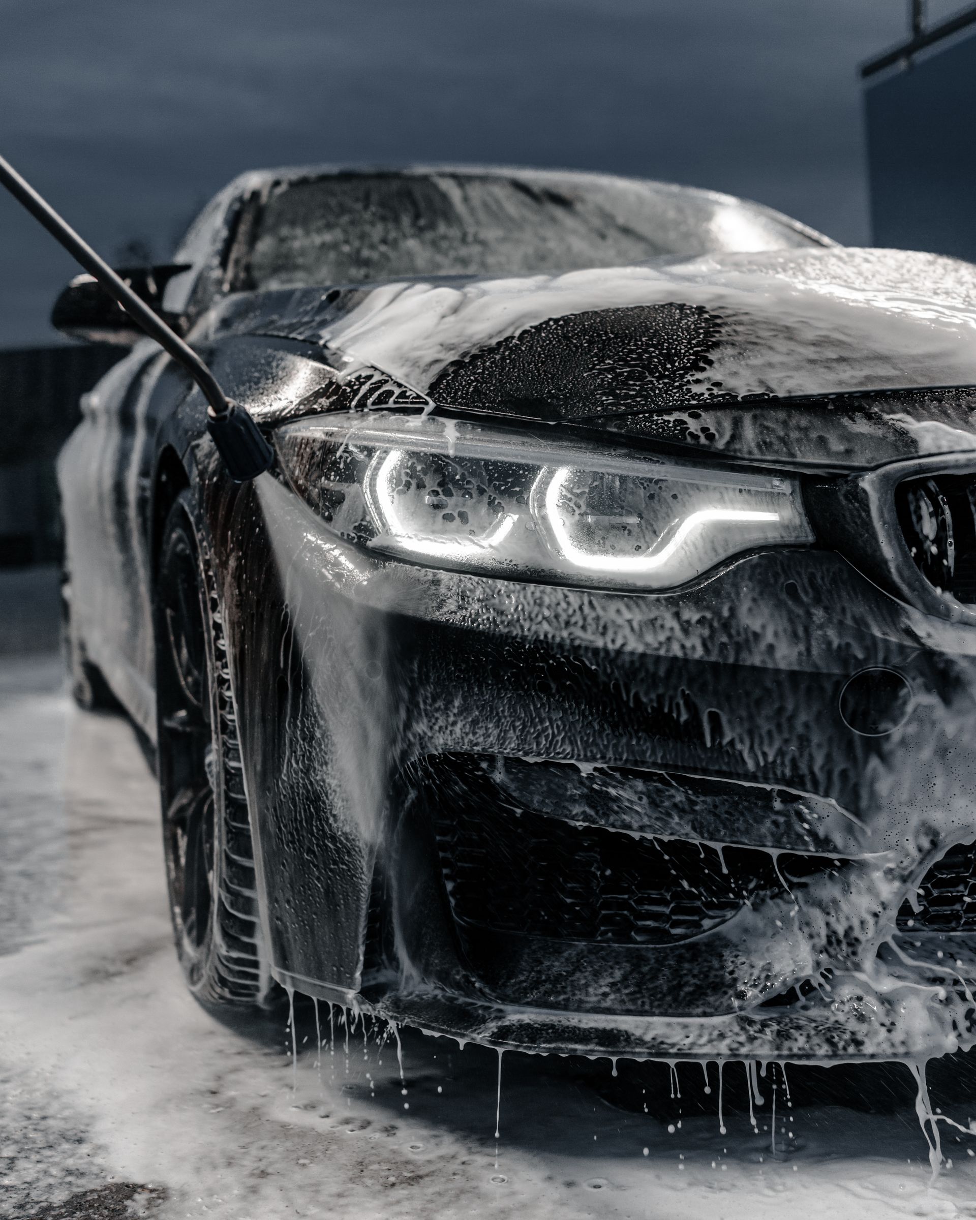 A close-up of a brush scrubbing a blue car with soapy water next to a red taillight.