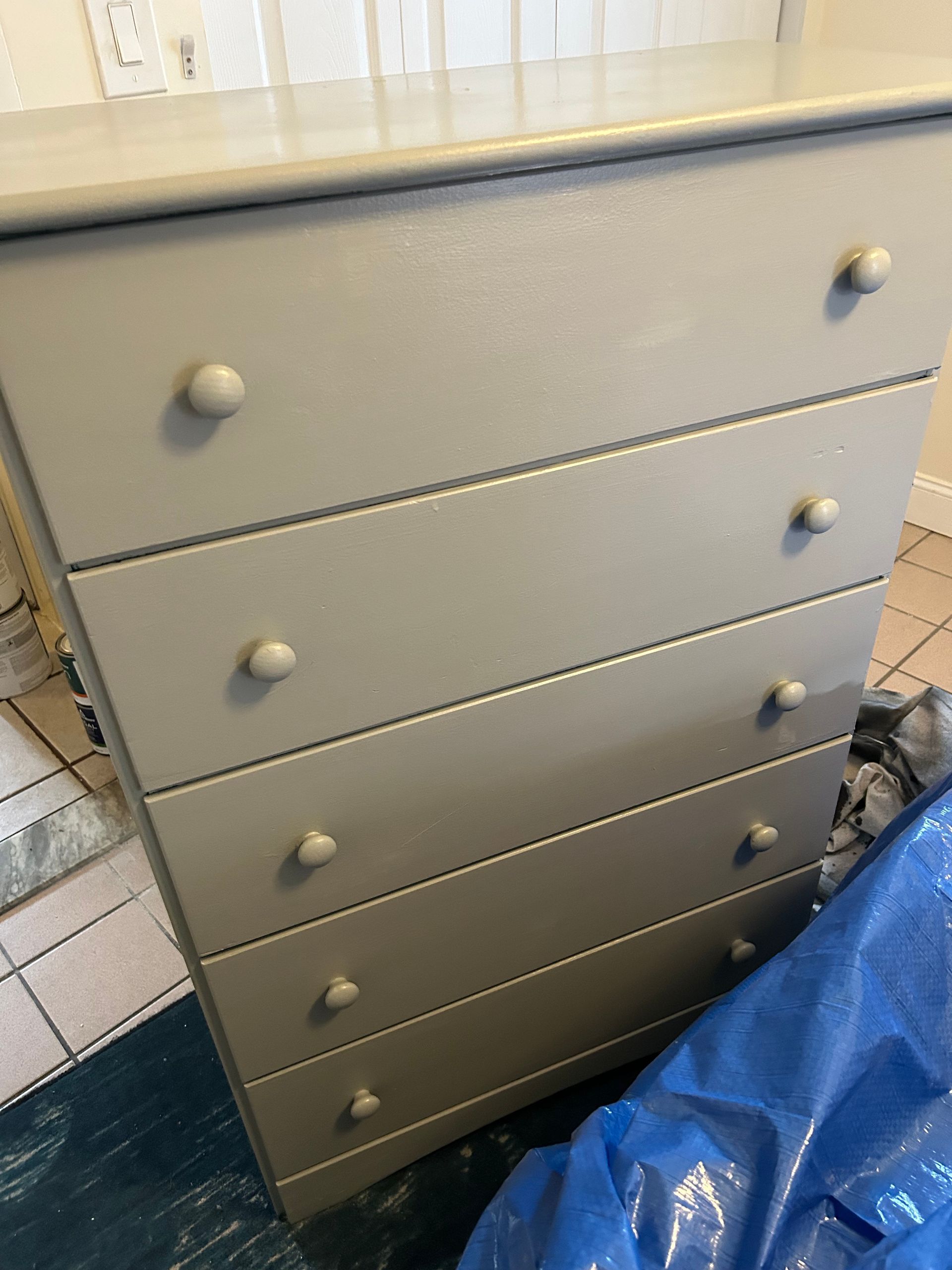 A dresser with four drawers is sitting next to a blue tarp.