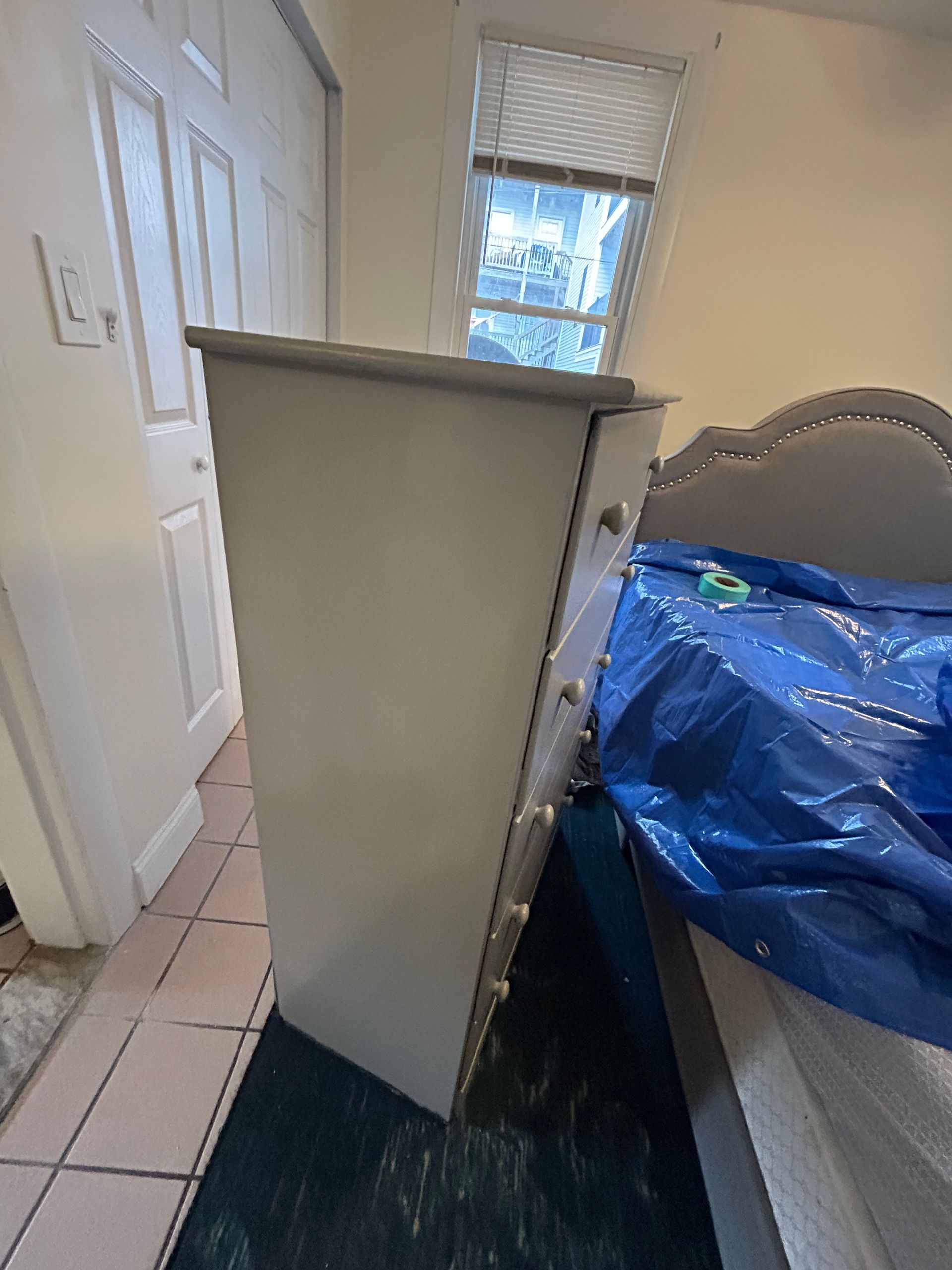 A white dresser is sitting next to a bed in a bedroom.