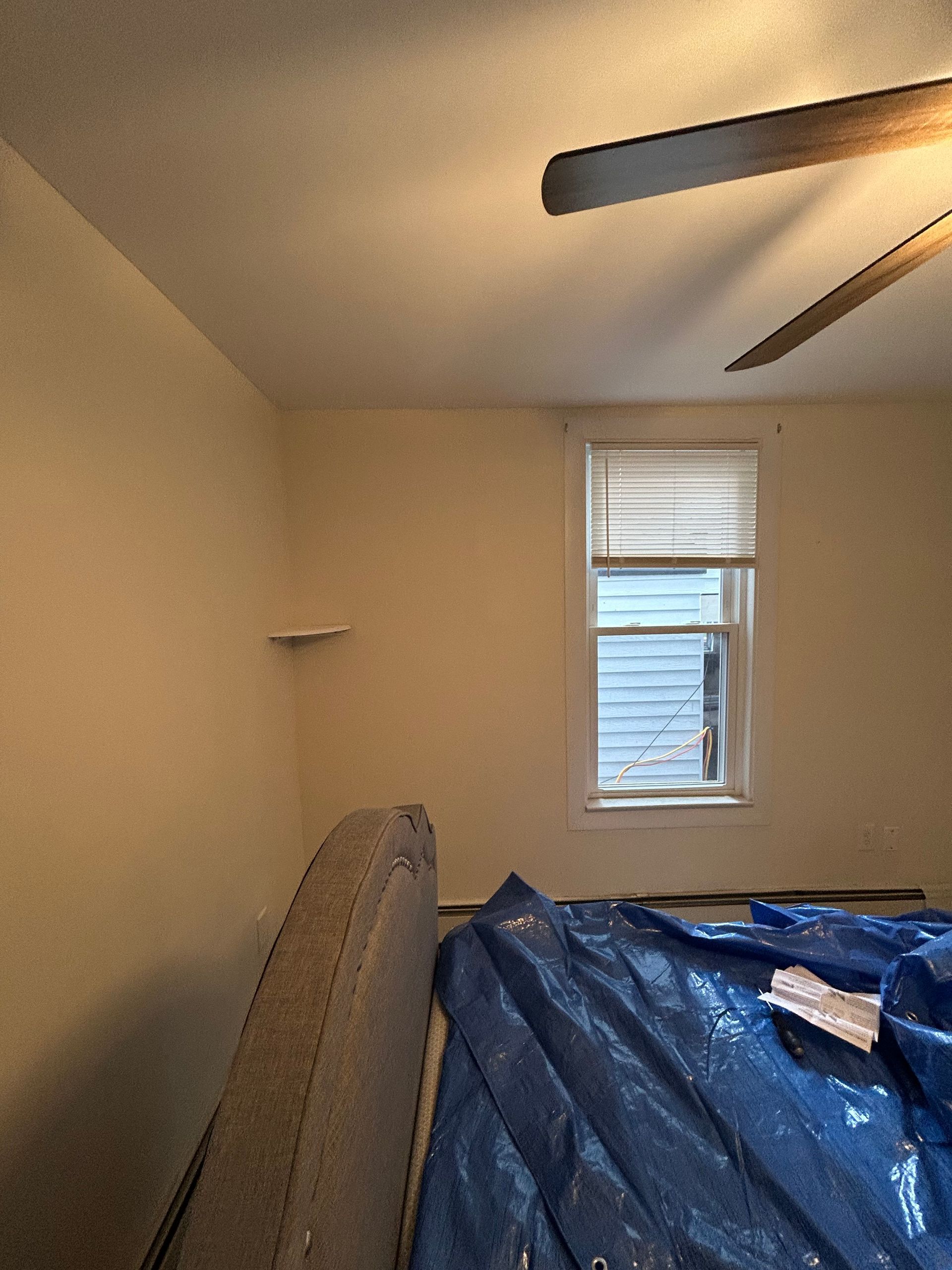 A bedroom with a blue tarp on the floor and a ceiling fan.