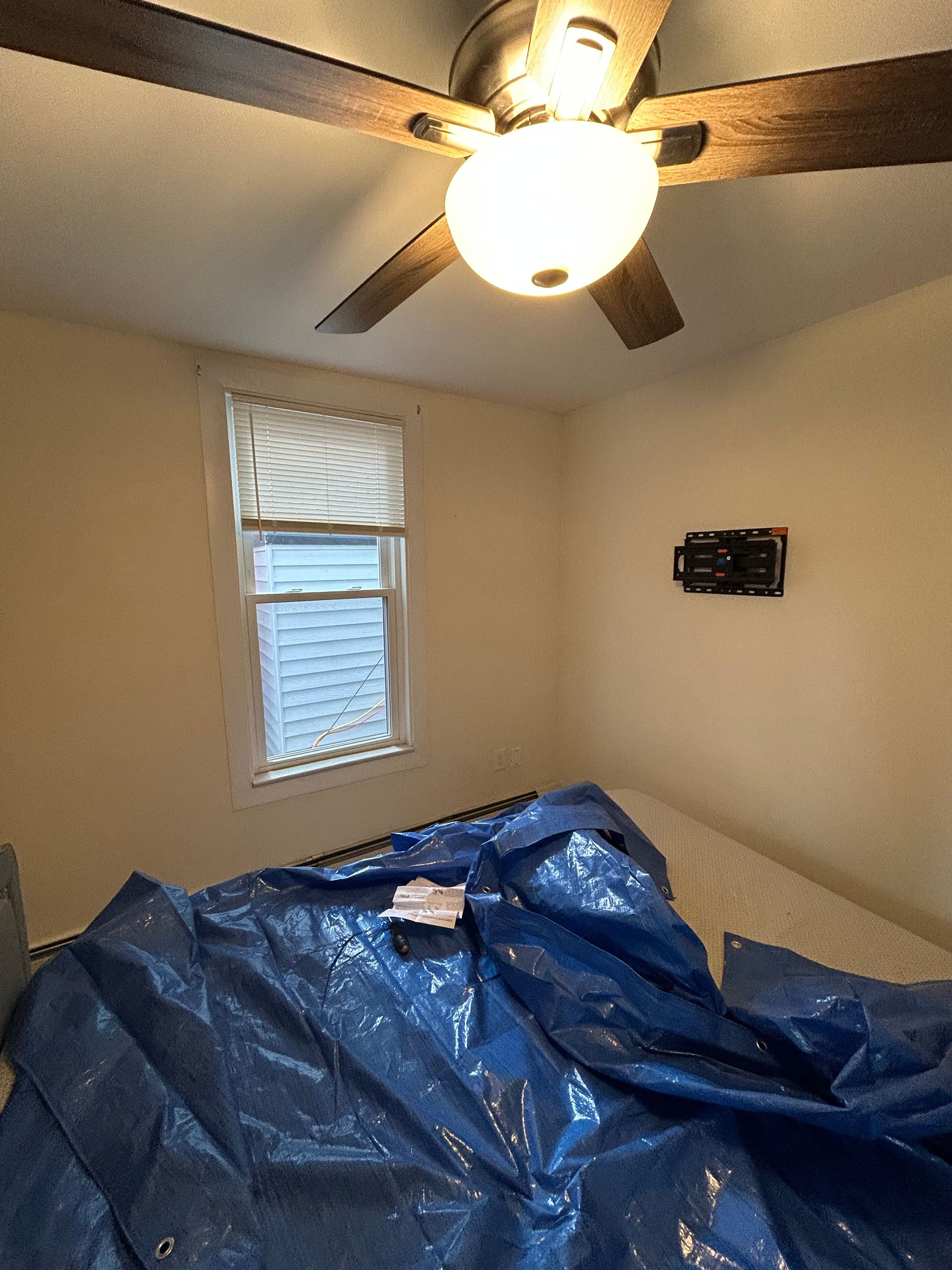 A bedroom with a blue tarp on the floor and a ceiling fan.