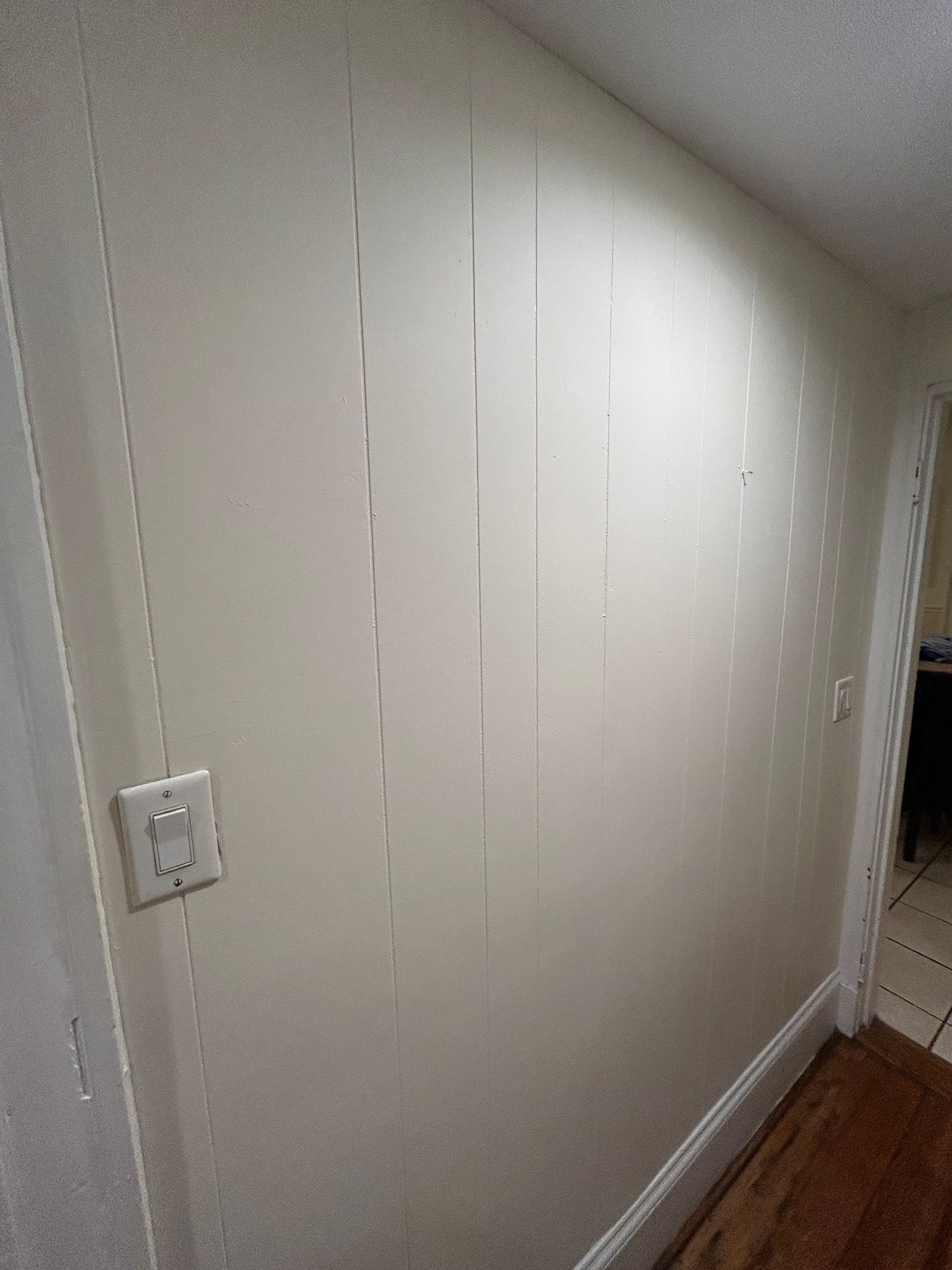 A hallway with a white wall and a wooden floor.